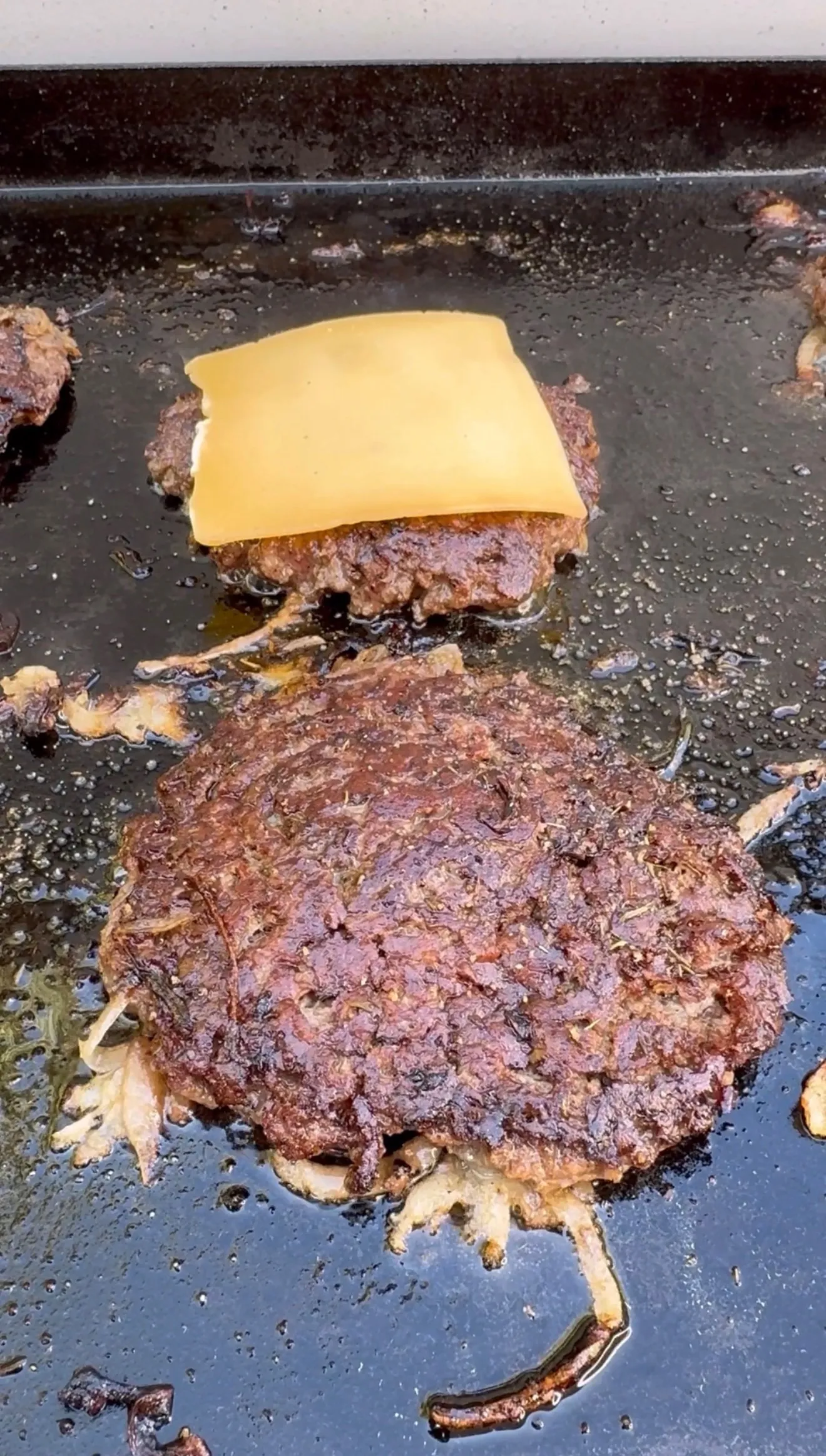 Smash burgers cooking on griddle with melted cheese