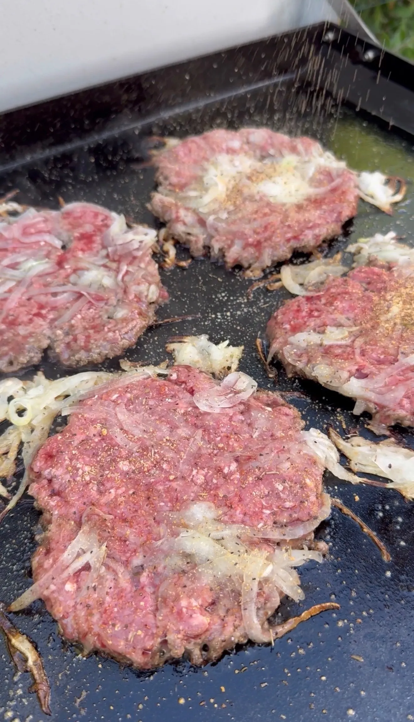 Smash burgers cooking on griddle with onions pressed in