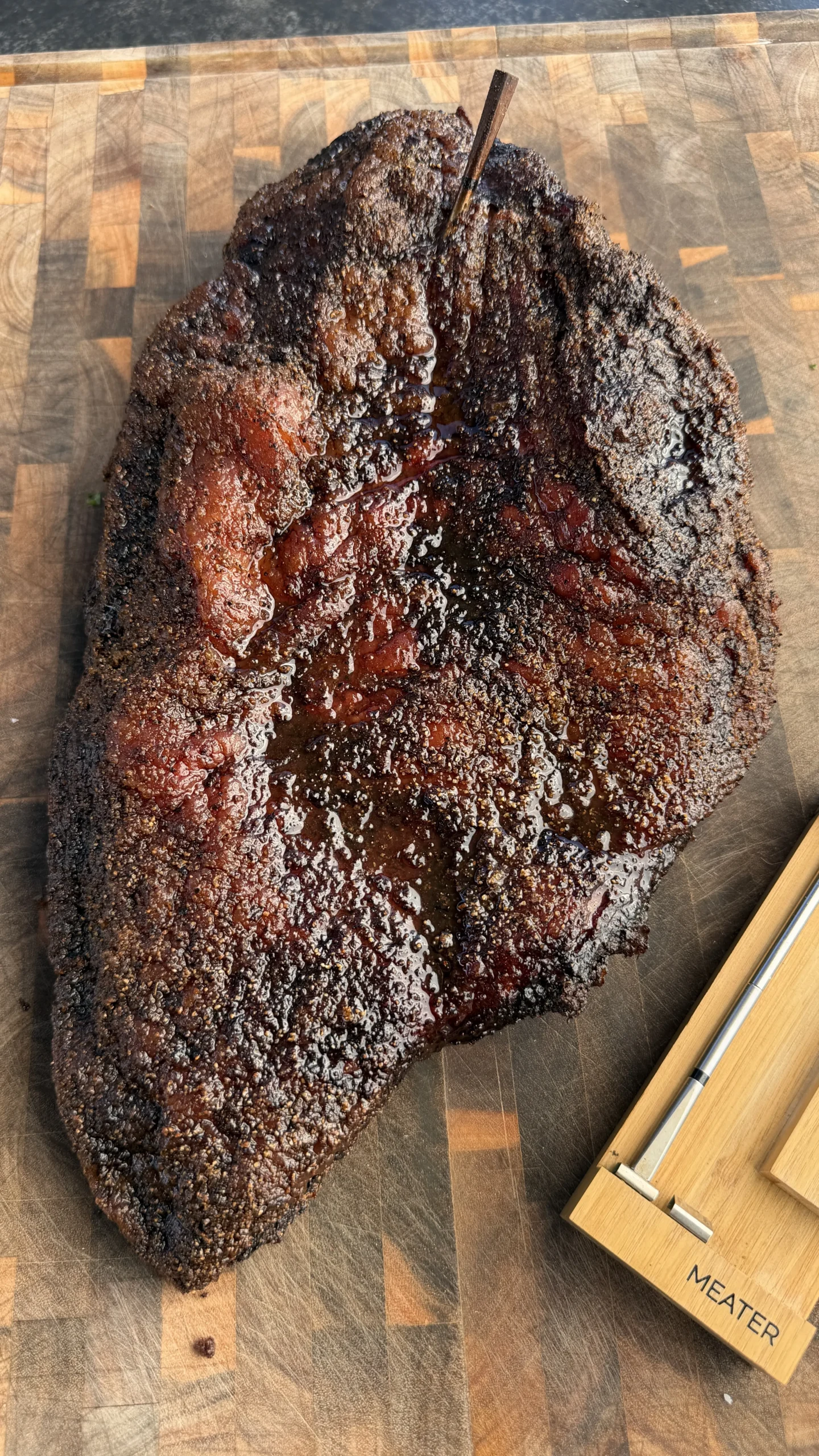 Smoked barbecue brisket with dark bark and meat thermometer on wooden cutting board