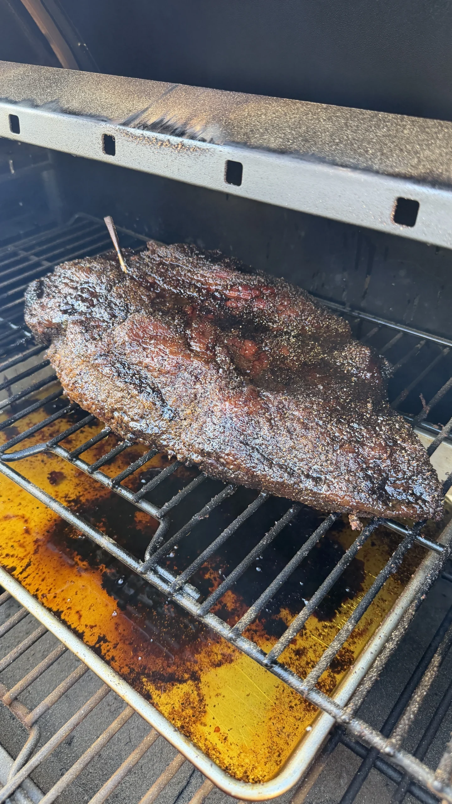 Dark crusted smoked barbecue brisket with meat thermometer cooking on smoker grates with yellow drip pan