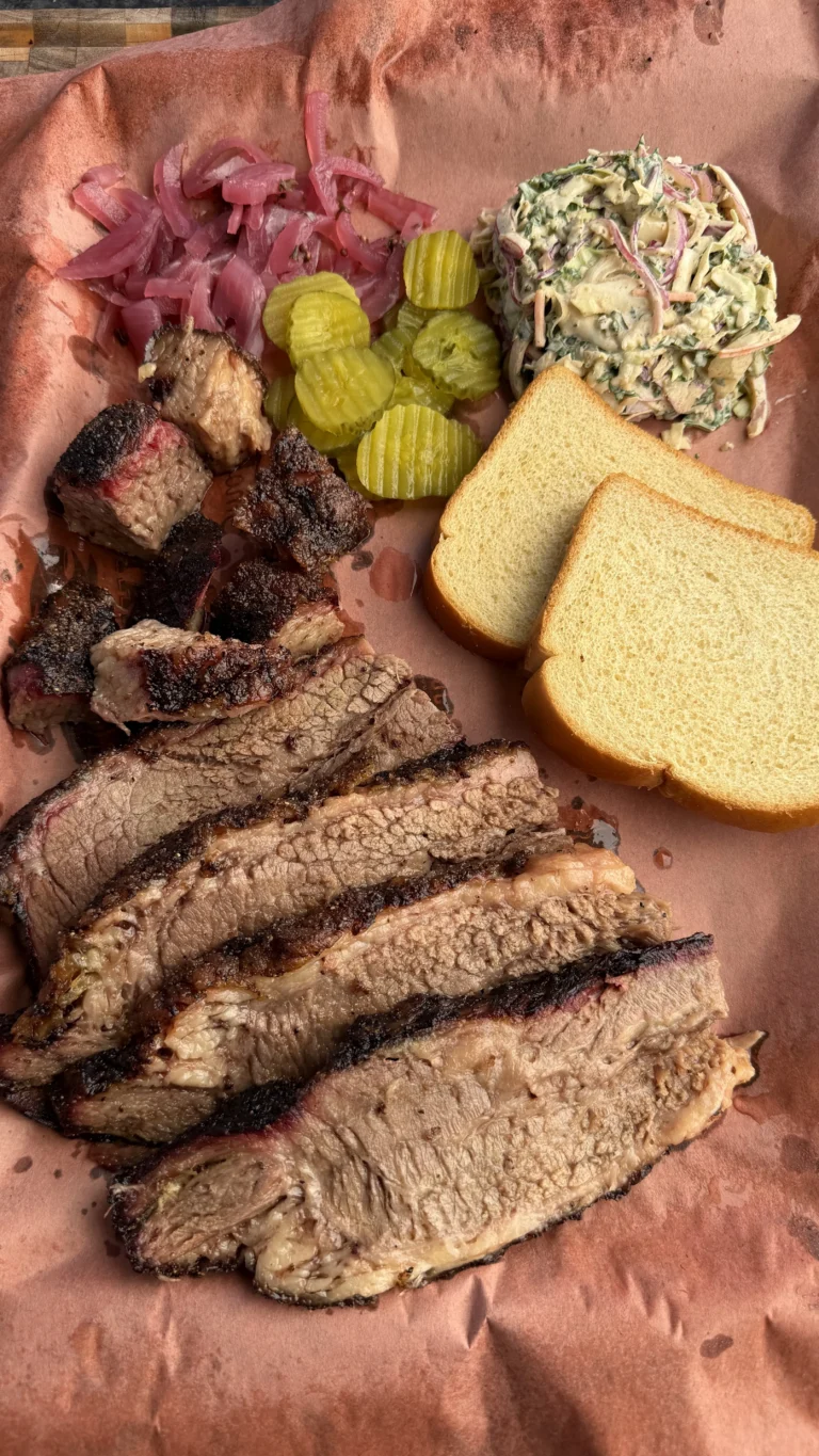 Sliced smoked barbecue brisket on butcher paper with pickles, coleslaw, burnt ends, and white bread