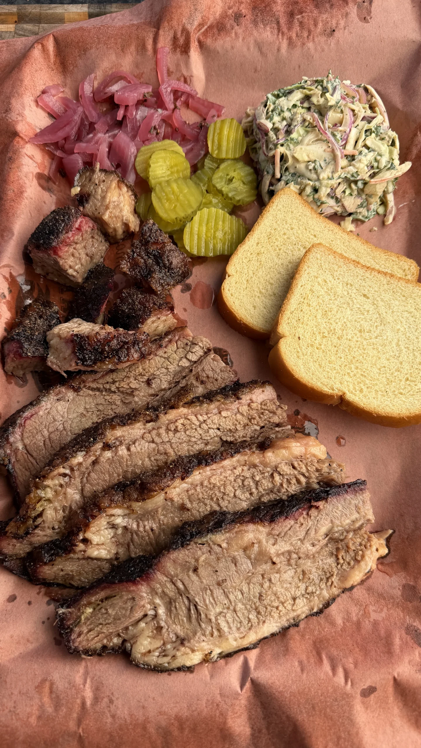 Sliced smoked barbecue brisket on butcher paper with pickles, coleslaw, burnt ends, and white bread