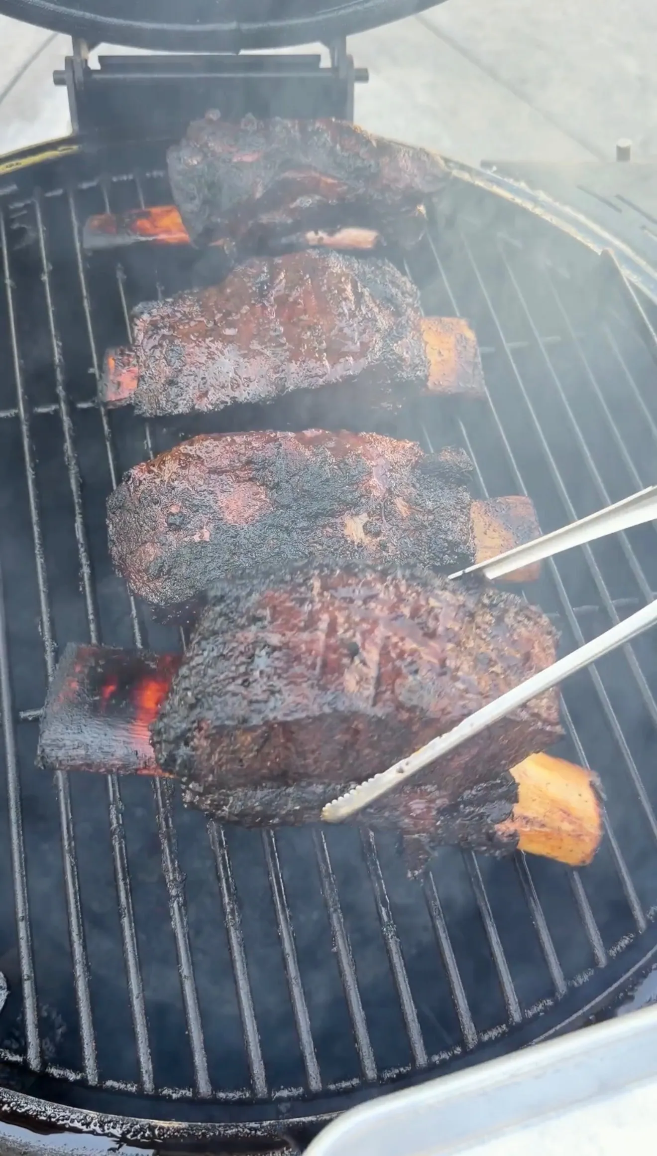 Smoked barbecue beef ribs with dark crust cooking on outdoor grill grates