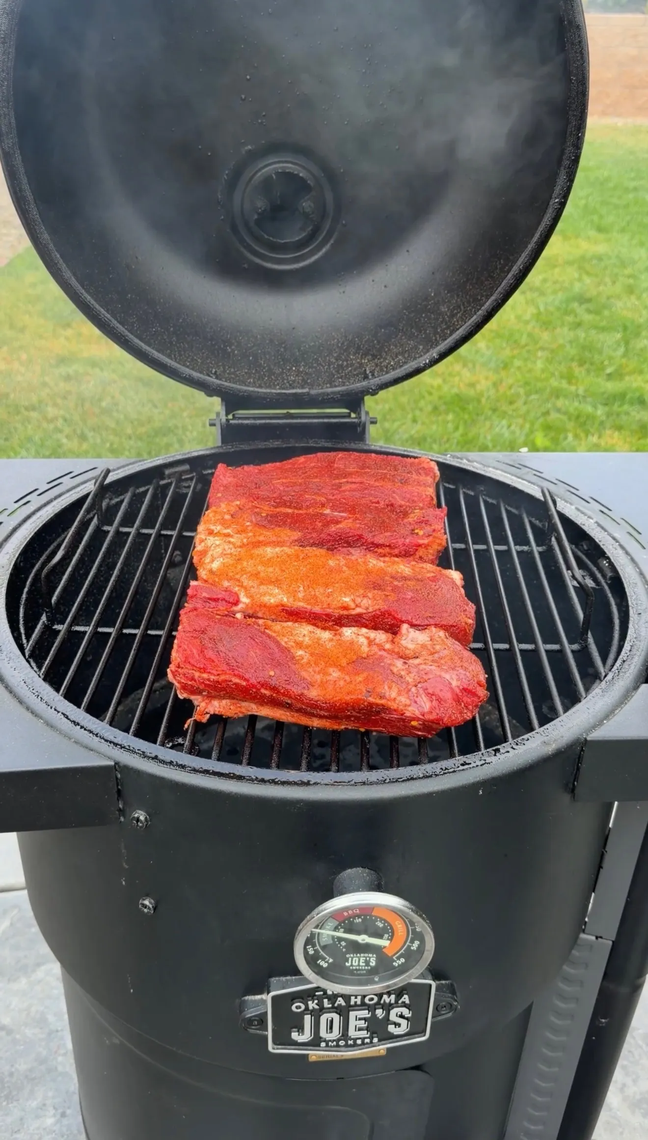Smoked barbecue beef ribs with red seasoning rub cooking on Oklahoma Joe's smoker grill grates