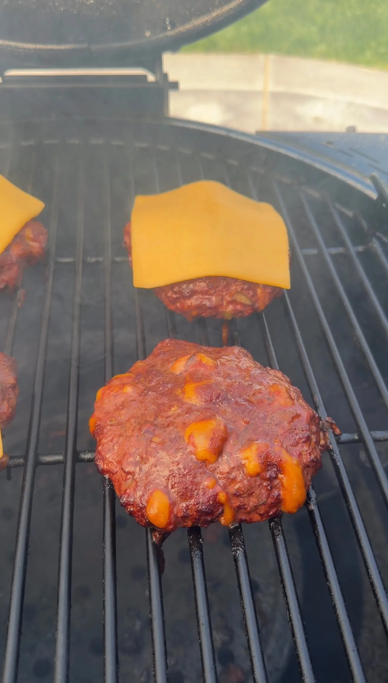 Smoked cheddar jalapeño stuffed burgers cooking on grill grates with melted cheese on top