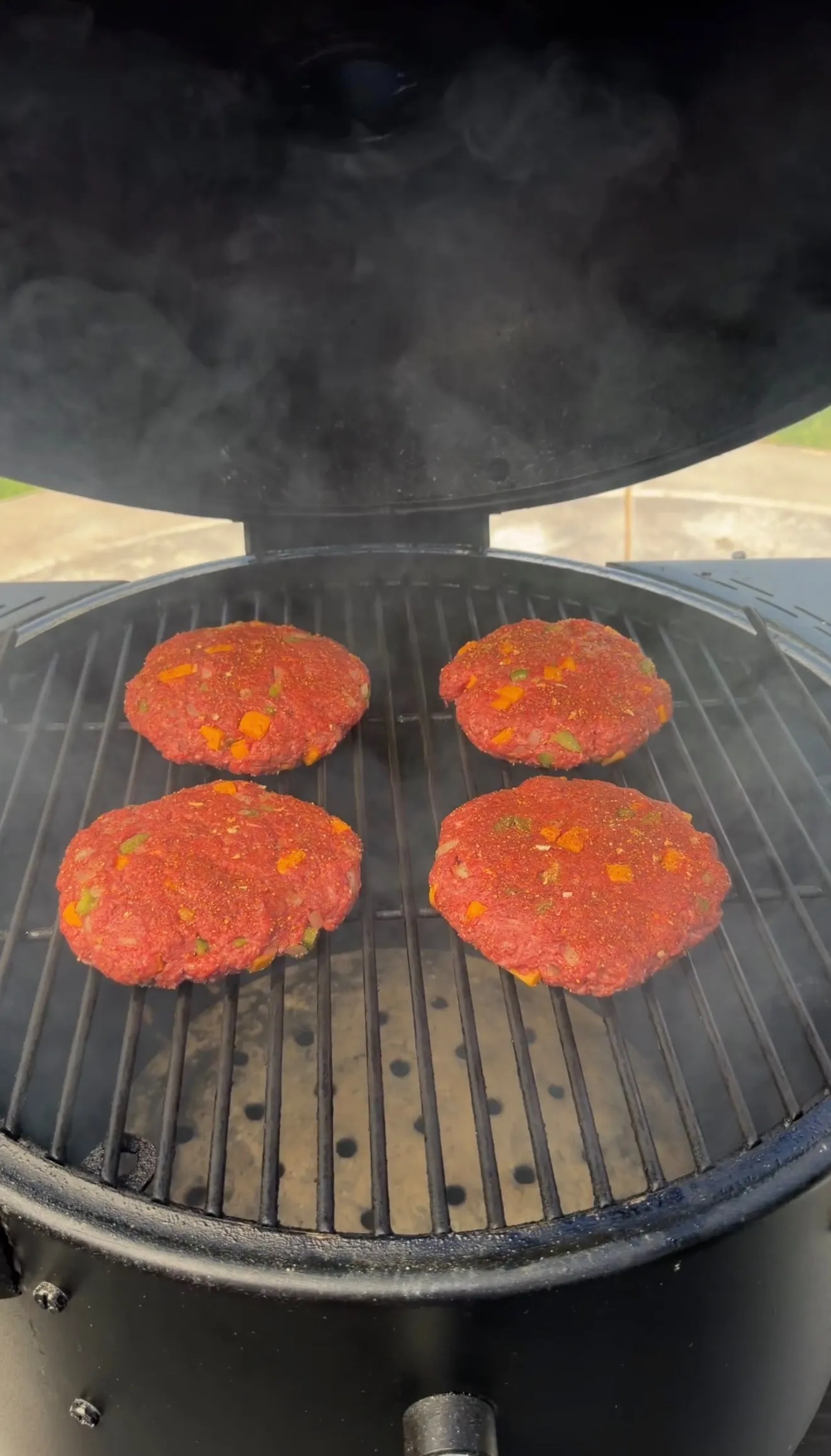 Four raw smoked cheddar jalapeño stuffed burger patties cooking on a kamado grill