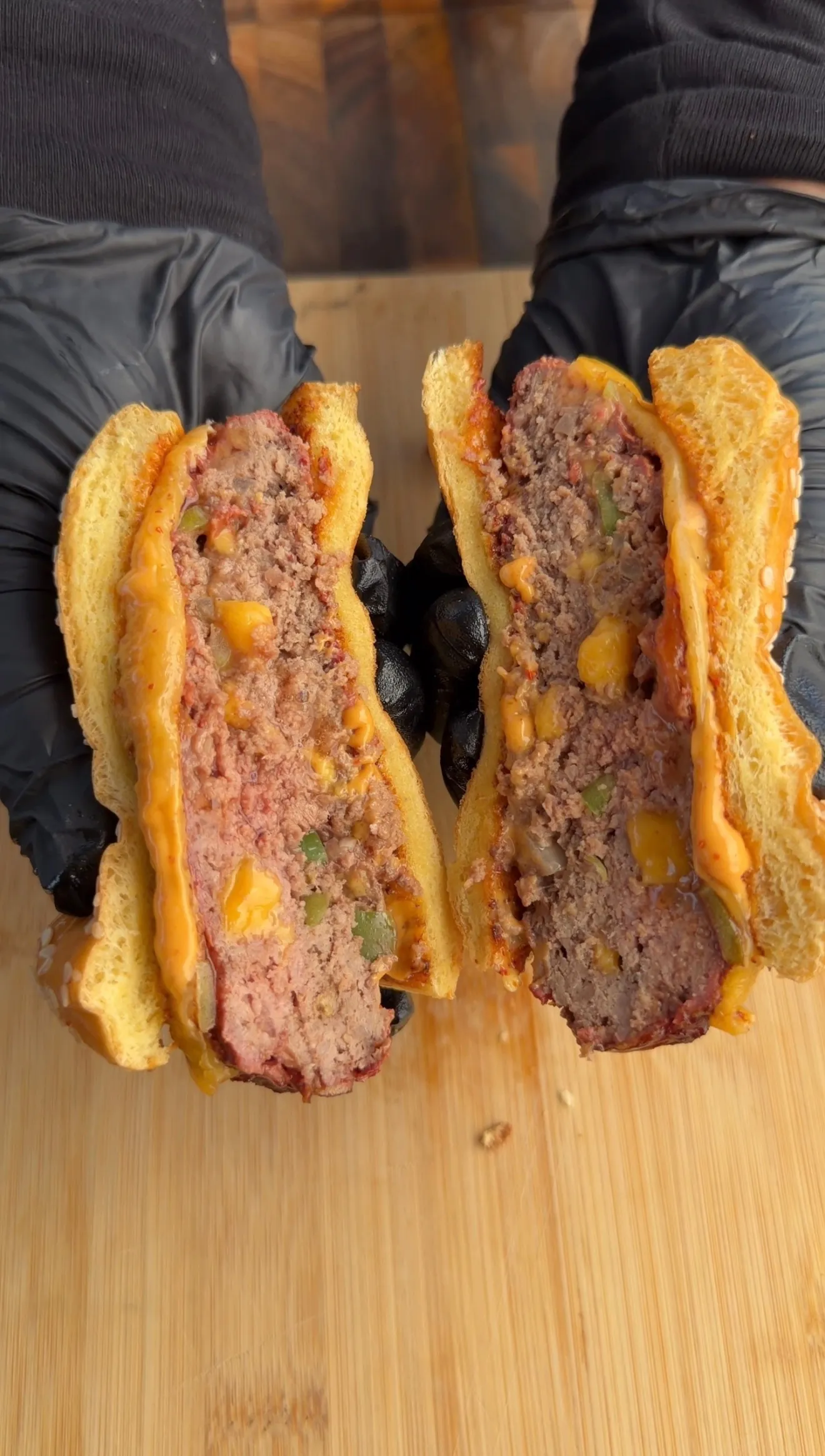 Two smoked cheddar jalapeño stuffed burgers cut in half showing melted cheese filling on wooden cutting board