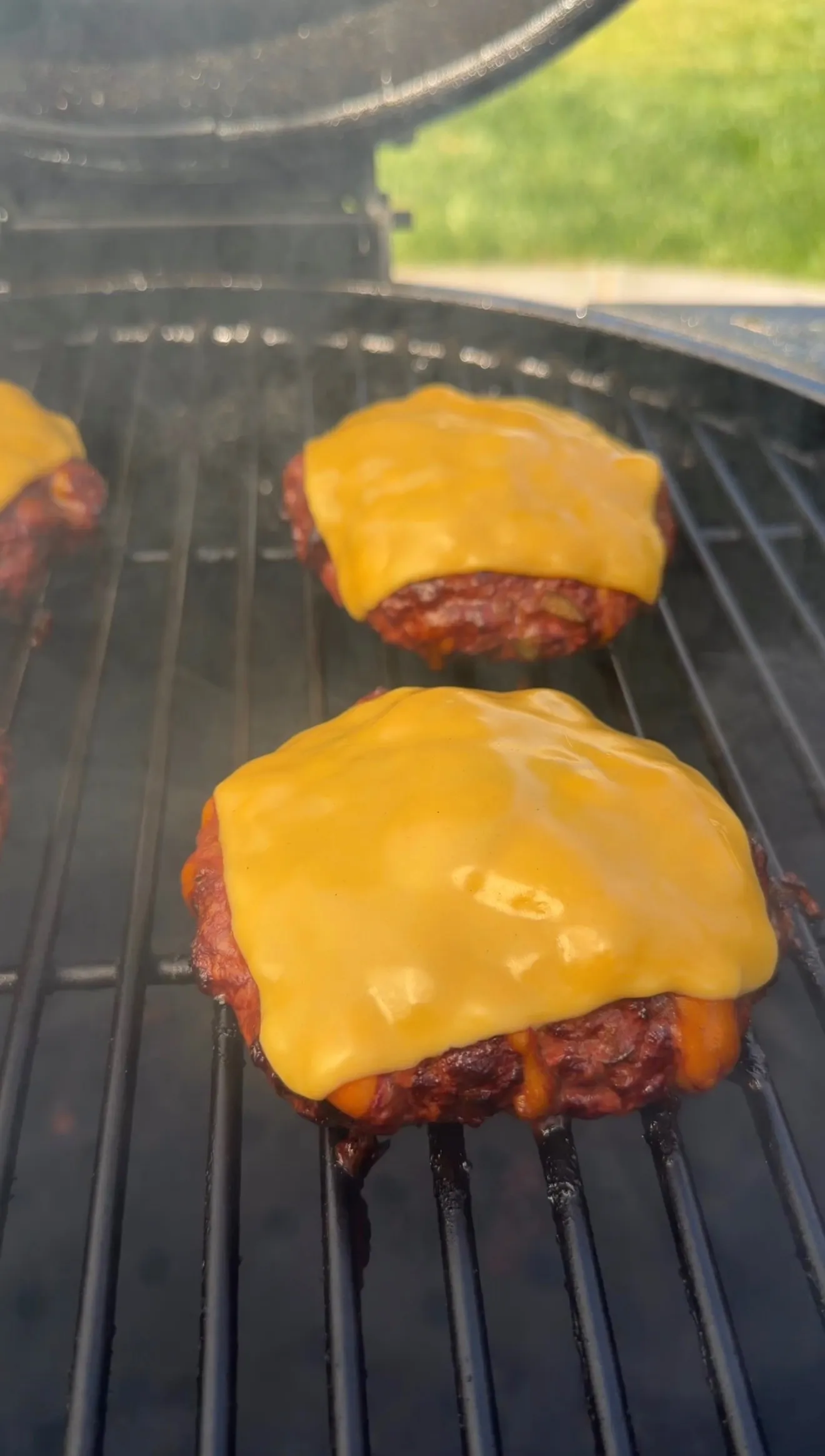 Two smoked cheddar jalapeño stuffed burgers with melted cheese on top cooking on a grill grate