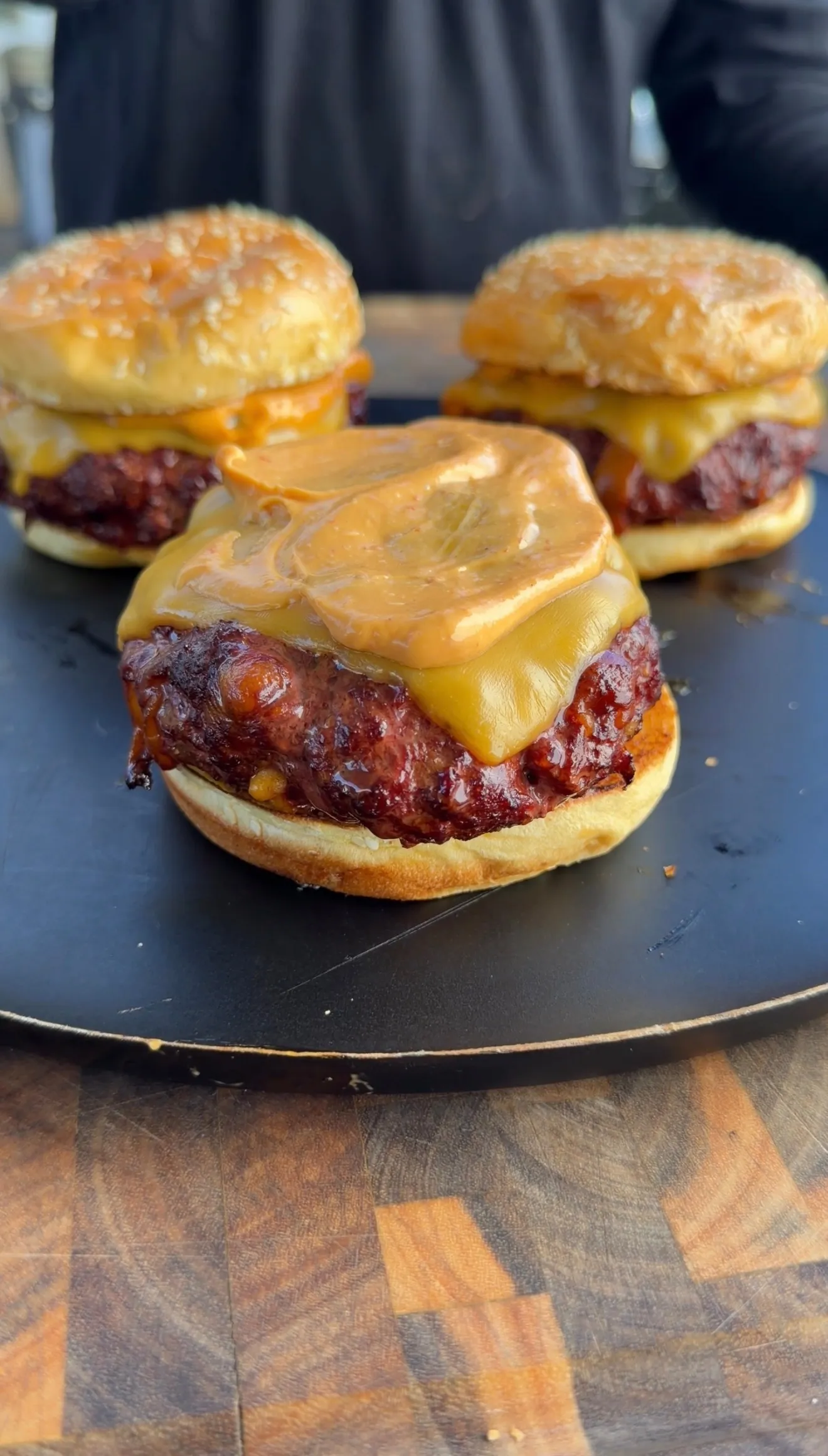 Three smoked cheddar jalapeño stuffed burgers with melted cheese on a dark cooking surface