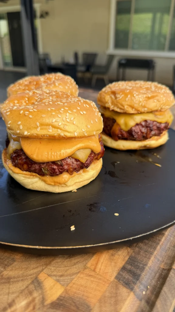 Two smoked cheddar jalapeño stuffed burgers with melted cheese on sesame seed buns on a dark serving plate