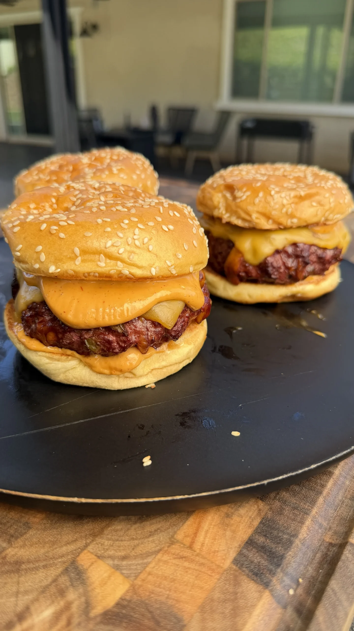 Two smoked cheddar jalapeño stuffed burgers with melted cheese on sesame seed buns on a dark serving plate