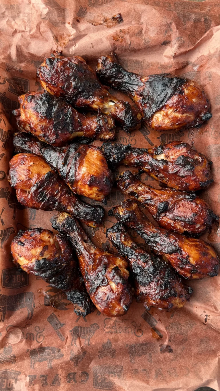 Grilled barbecue chicken drumsticks with charred skin and caramelized glaze on brown butcher paper