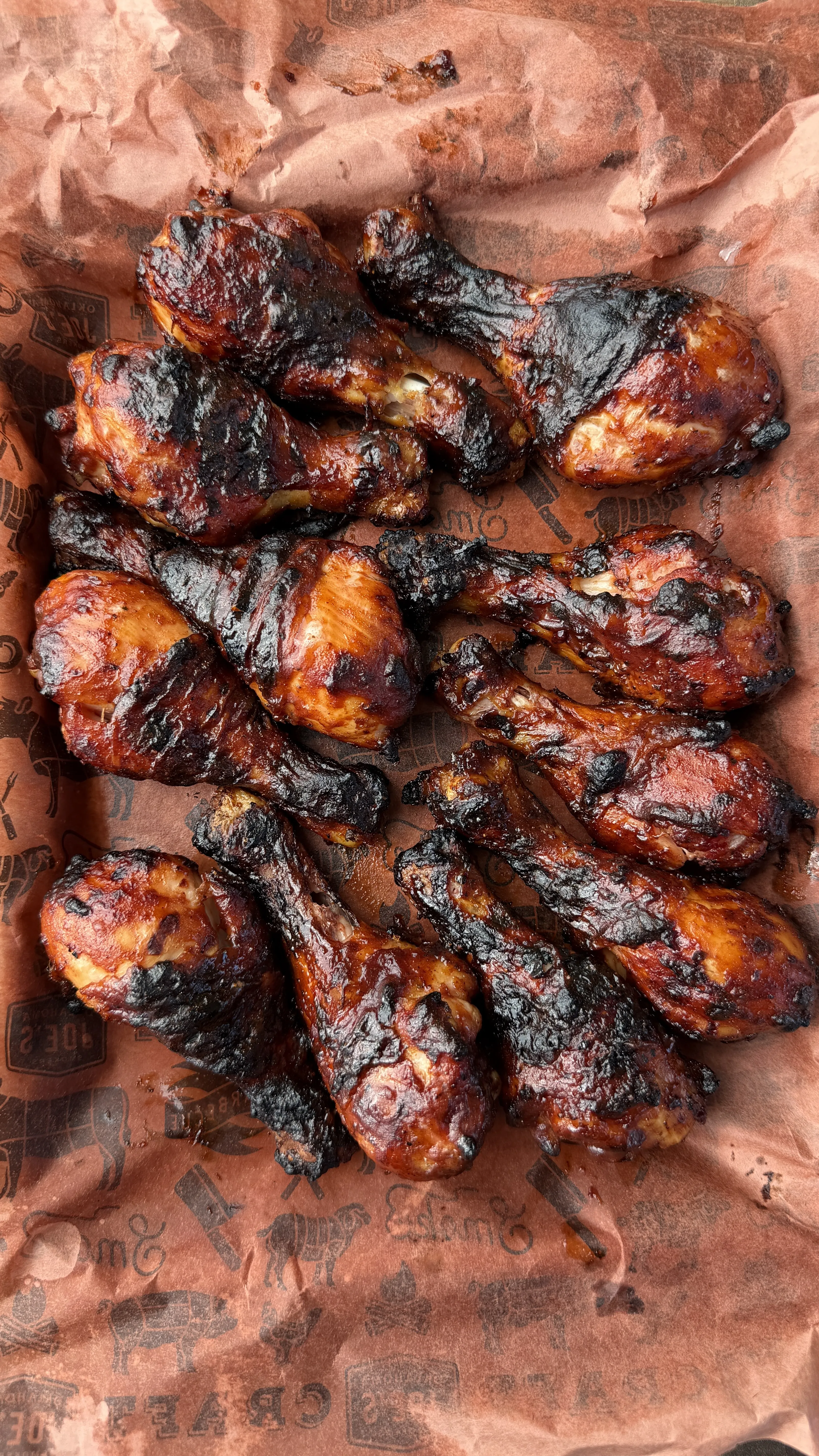 Grilled barbecue chicken drumsticks with charred skin and caramelized glaze on brown butcher paper