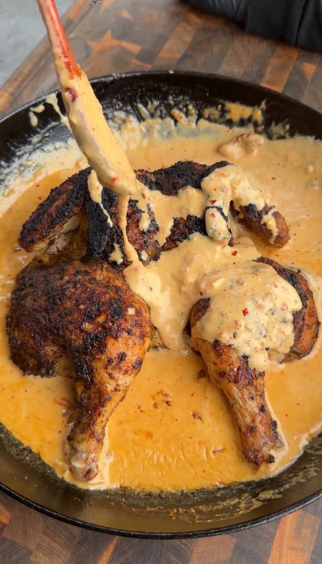 Golden spatchcock chicken with creamy marry me sauce being spooned over in black cast iron skillet