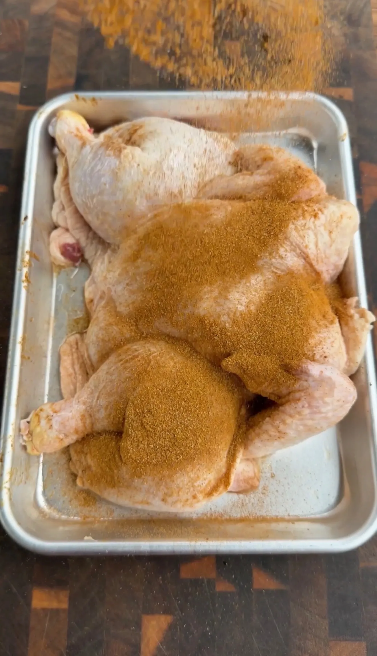 Raw spatchcock chicken seasoned with spices in a metal baking pan ready for roasting