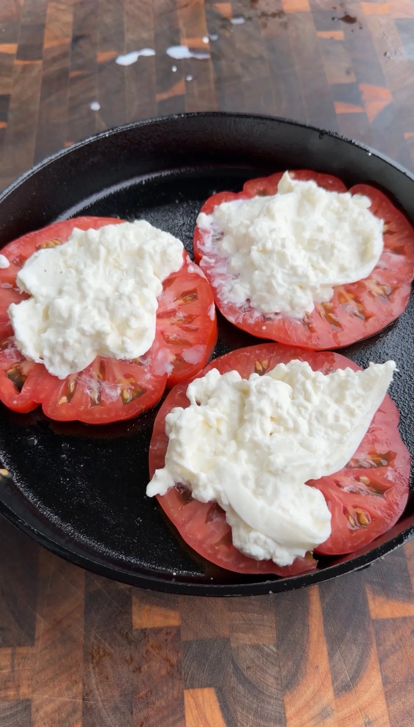 Three halved tomatoes stuffed with white ricotta cheese cooking in a black cast iron skillet