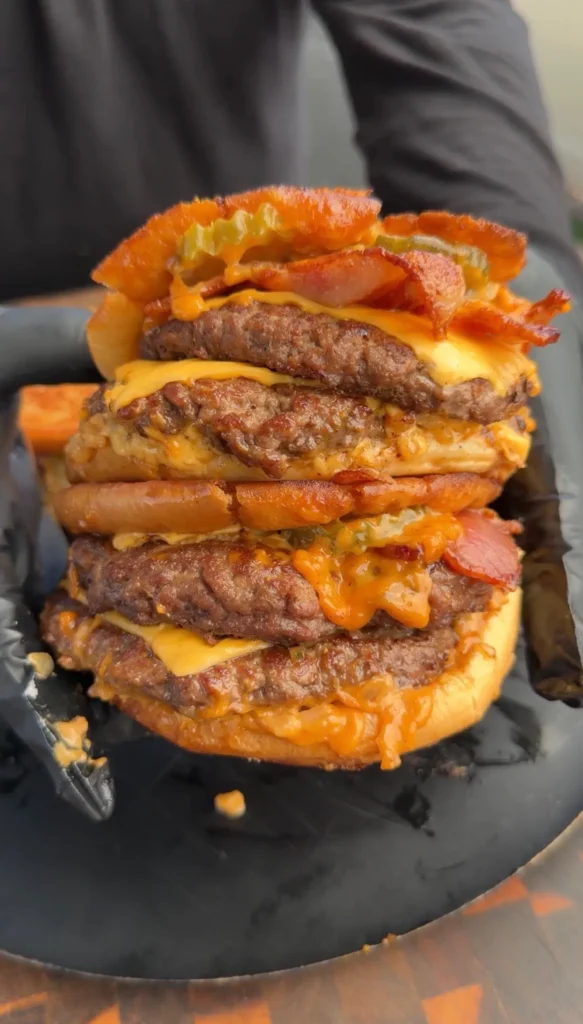 Towering bacon cheeseburger patty melt with multiple beef patties, melted cheese, and bacon on a dark plate