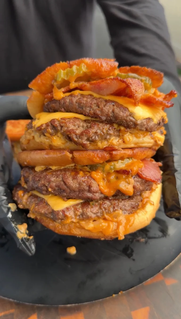 Towering bacon cheeseburger patty melt with multiple beef patties, melted cheese, and bacon on a dark plate