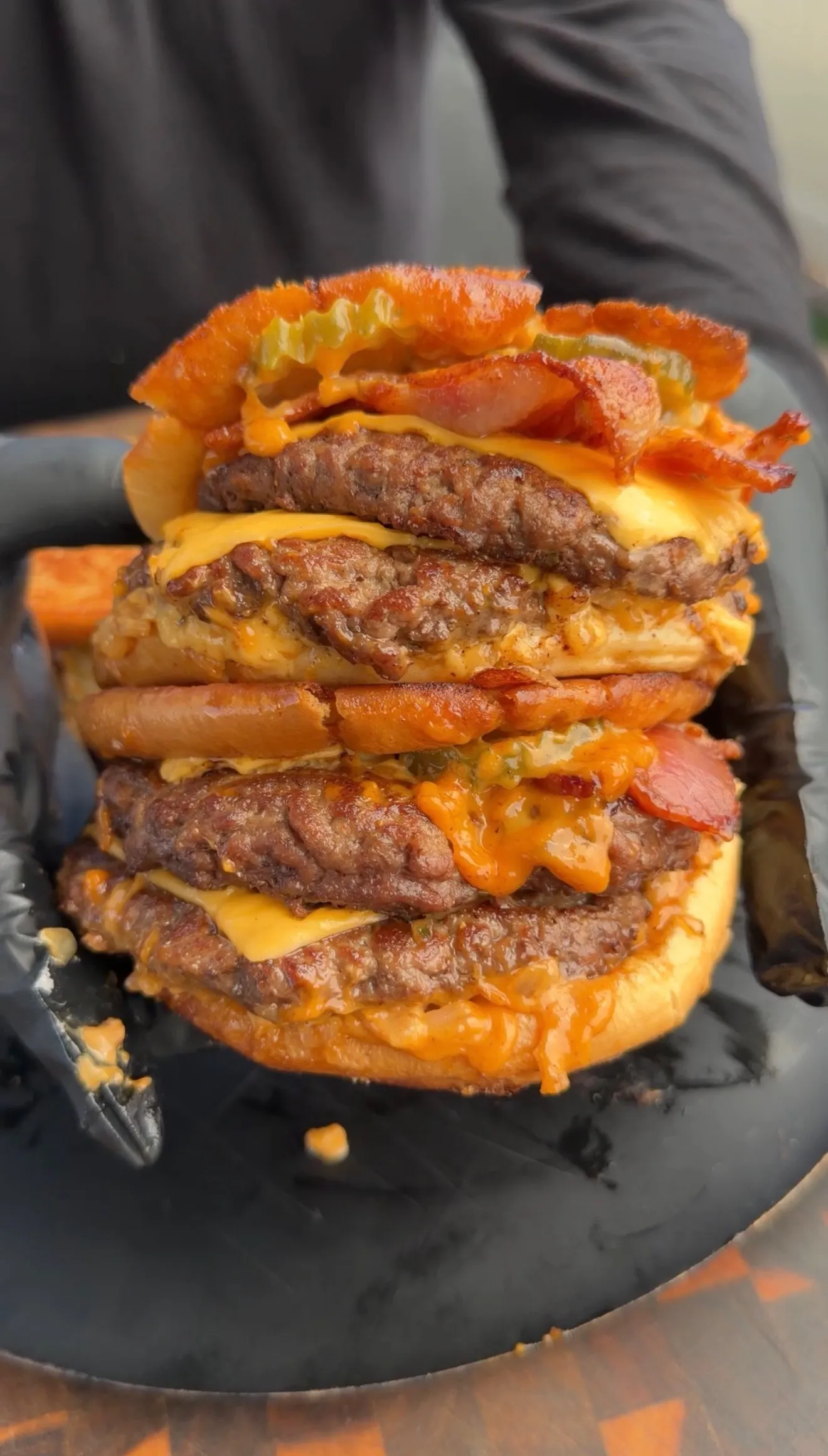Towering bacon cheeseburger patty melt with multiple beef patties, melted cheese, and bacon on a dark plate