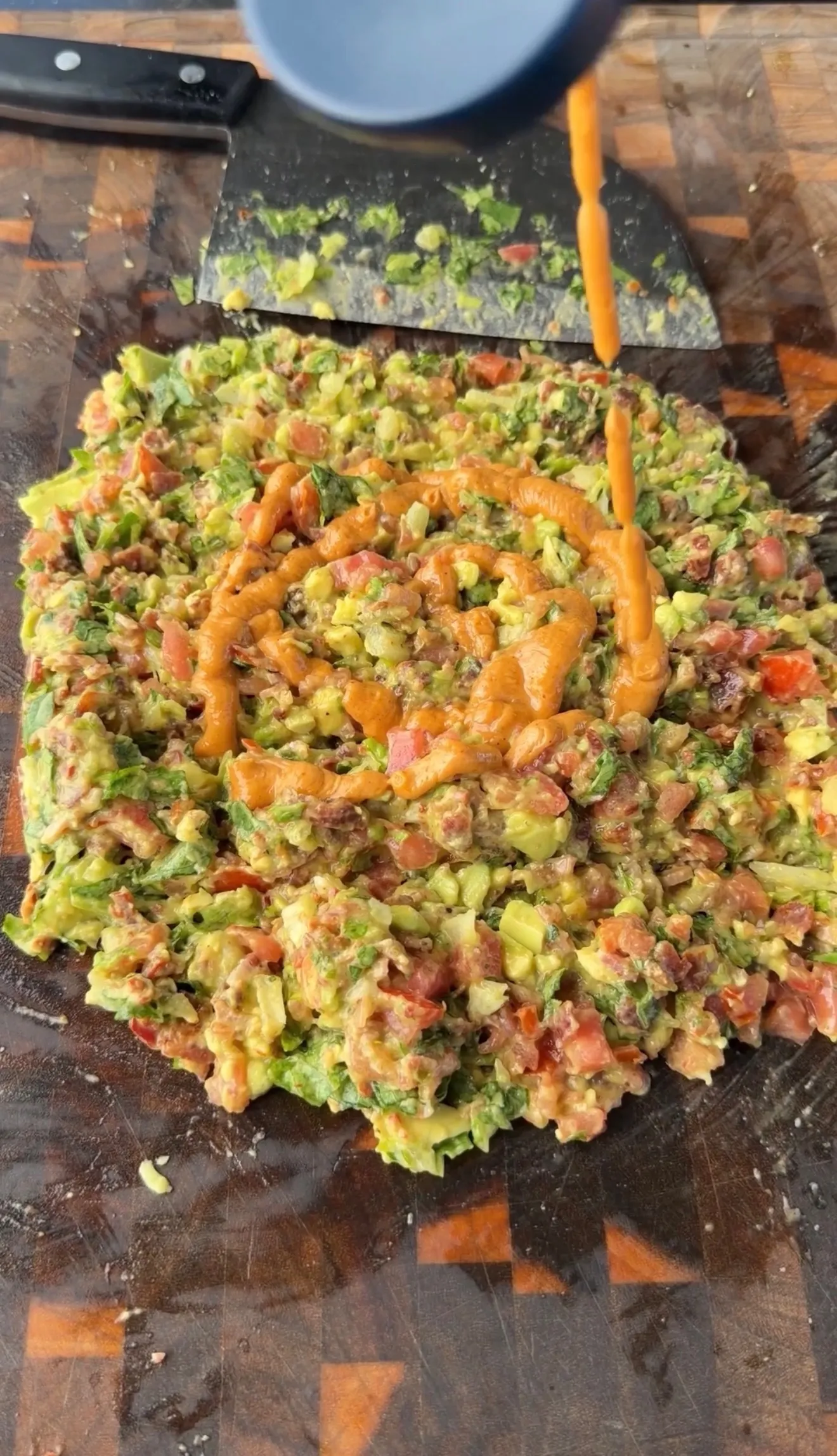 Freshly chopped avocado BLT slider mixture with tomatoes, herbs, and a drizzle of chipotle sauce on a wooden board