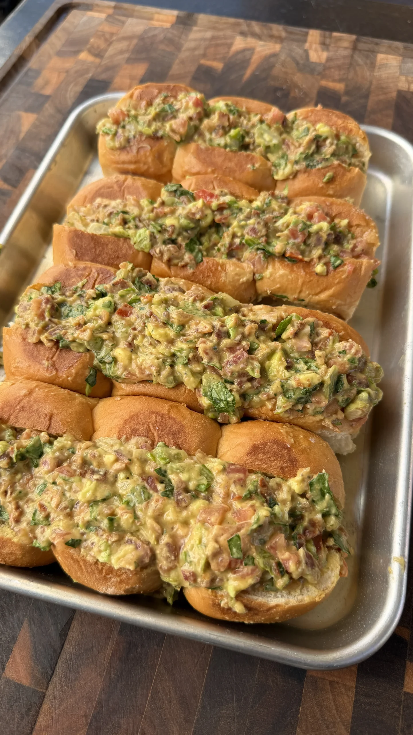Avocado BLT chopped sliders topped with chunky guacamole, bacon, and herbs on toasted rolls in a metal tray