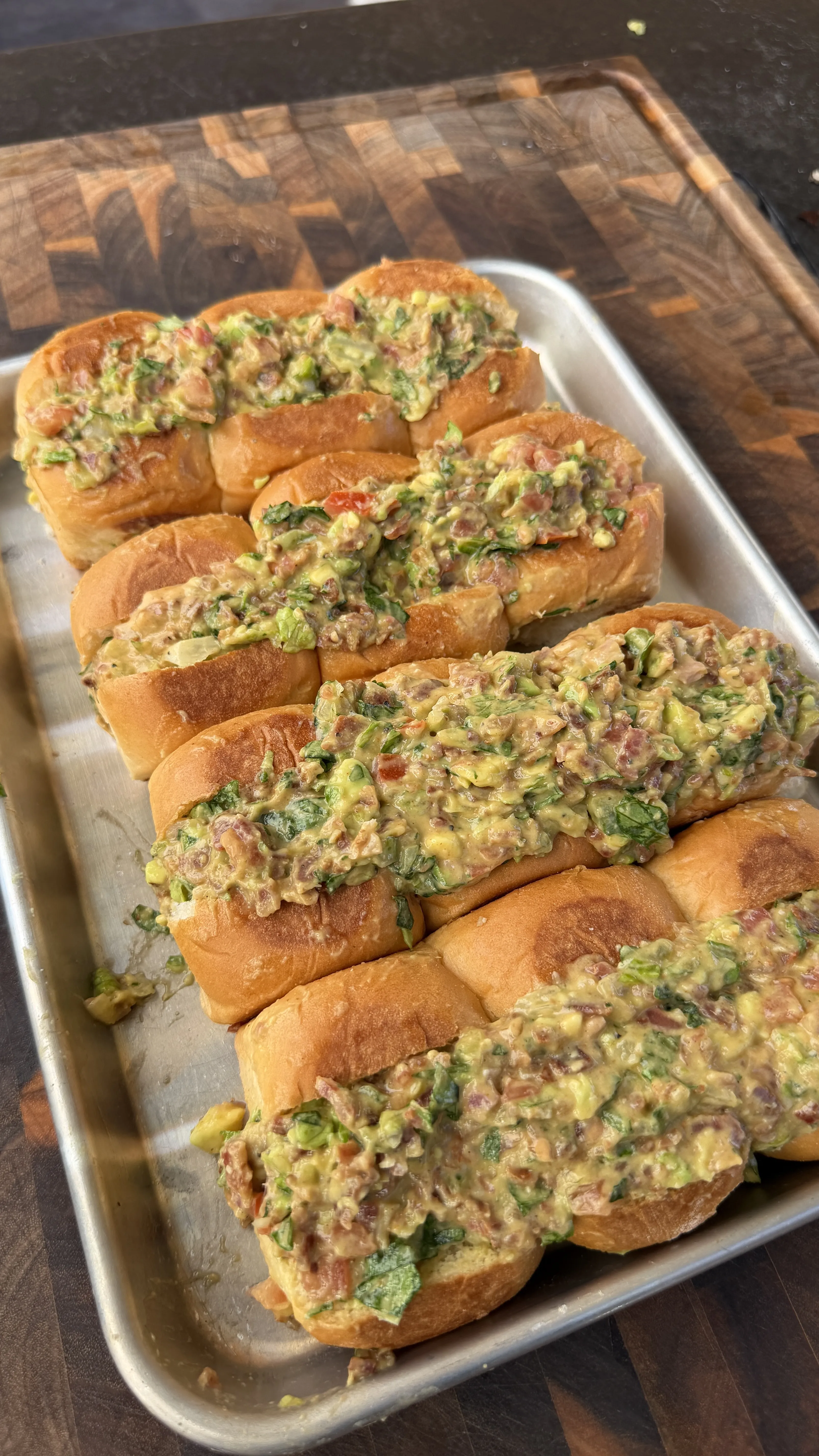Avocado BLT chopped sliders on a silver baking sheet, topped with chunky guacamole bacon mixture on soft rolls