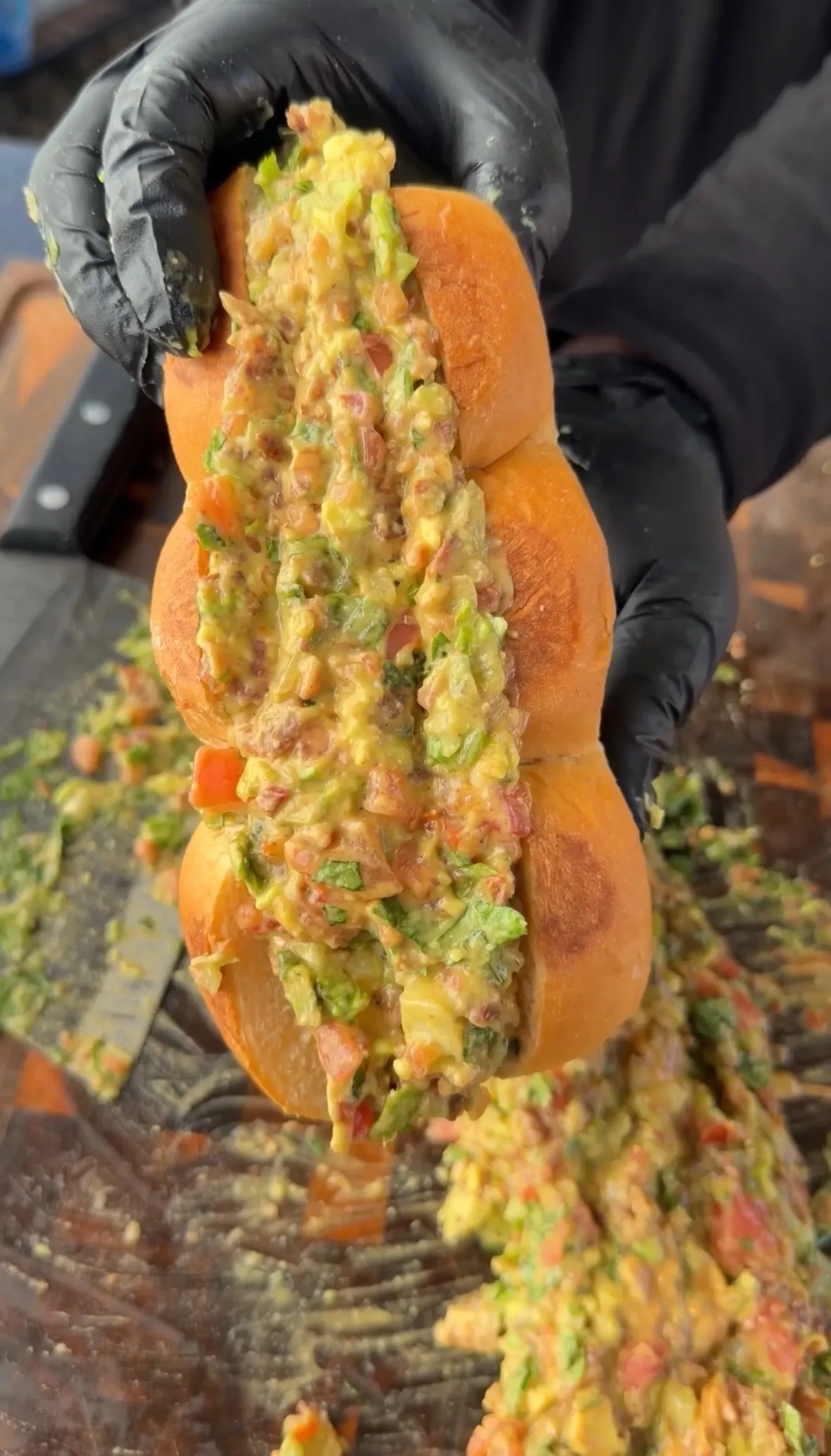 Hands holding brioche slider buns overflowing with chunky avocado BLT chopped filling with tomatoes and herbs