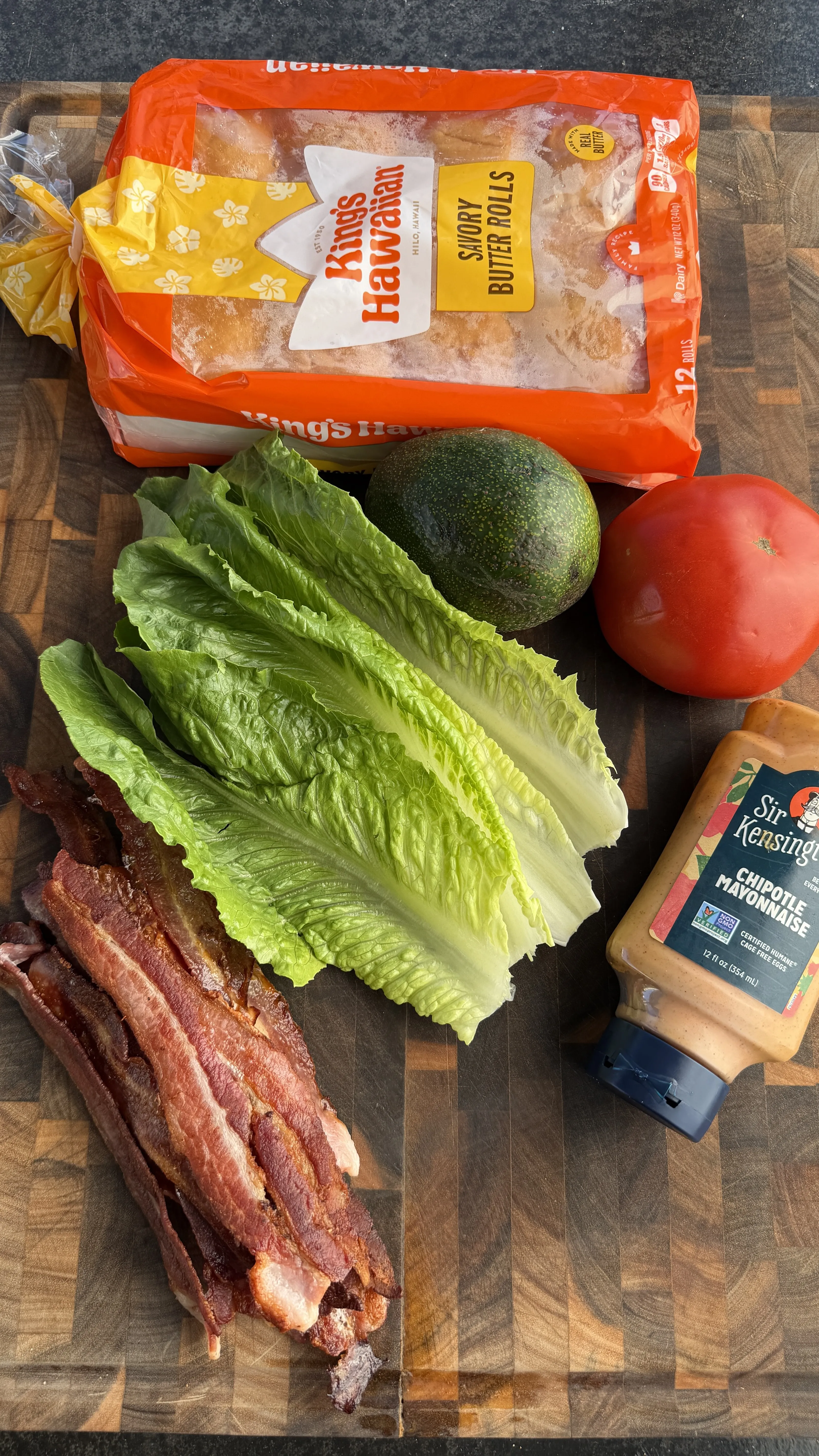 Avocado BLT slider ingredients: Kings Hawaiian rolls, romaine lettuce, avocado, tomato, bacon, and chipotle mayo on a wood board