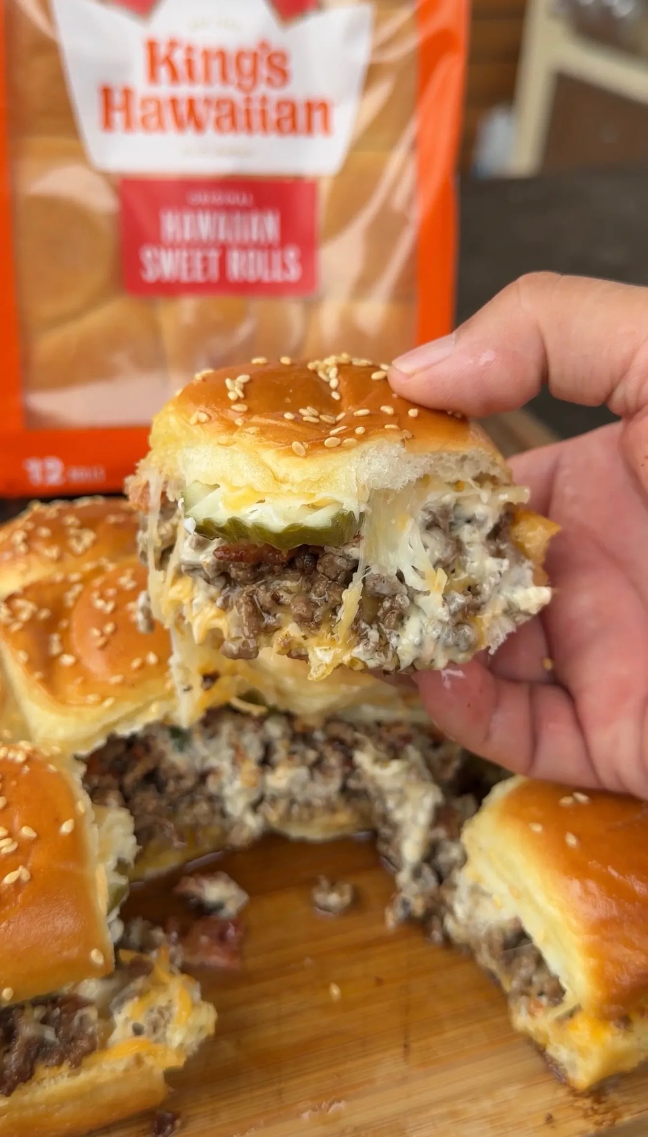 Hand holding a bacon cheeseburger pickle ranch slider with melted cheese and beef patty on sesame seed bun