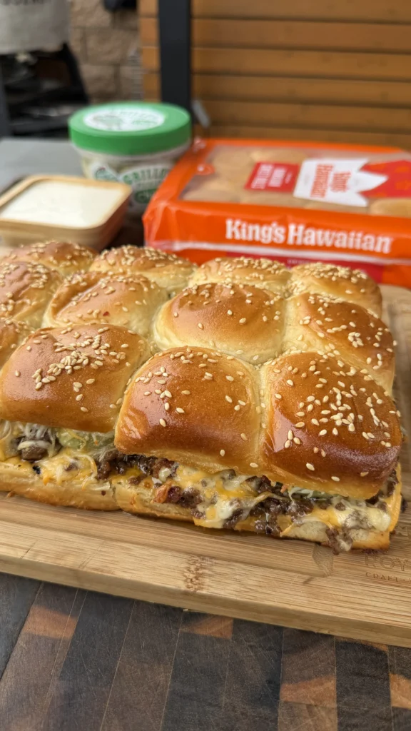 Six bacon cheeseburger pickle ranch sliders with sesame seed buns on a wooden cutting board