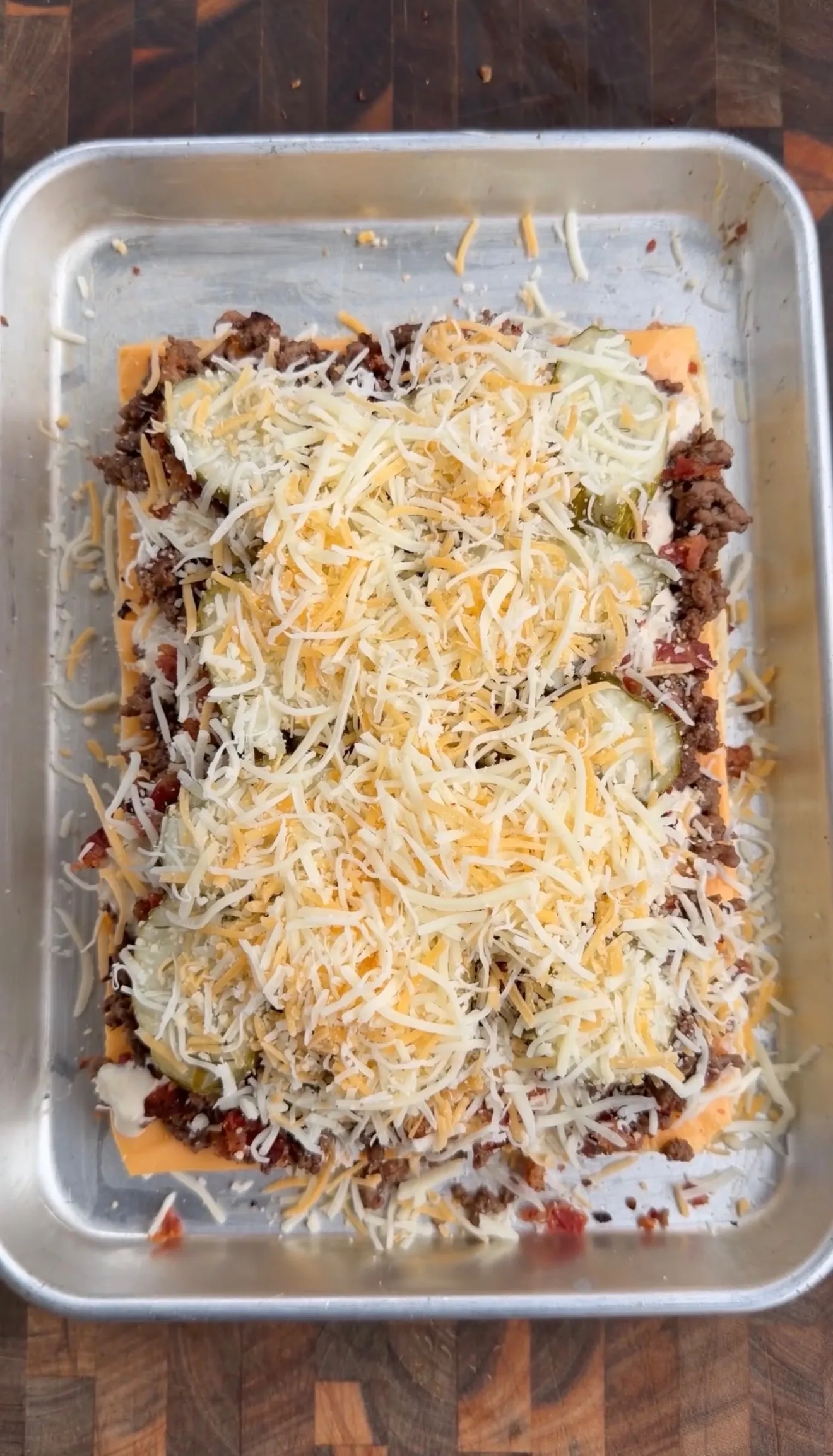 Bacon cheeseburger pickle ranch sliders casserole topped with shredded cheese in aluminum baking pan