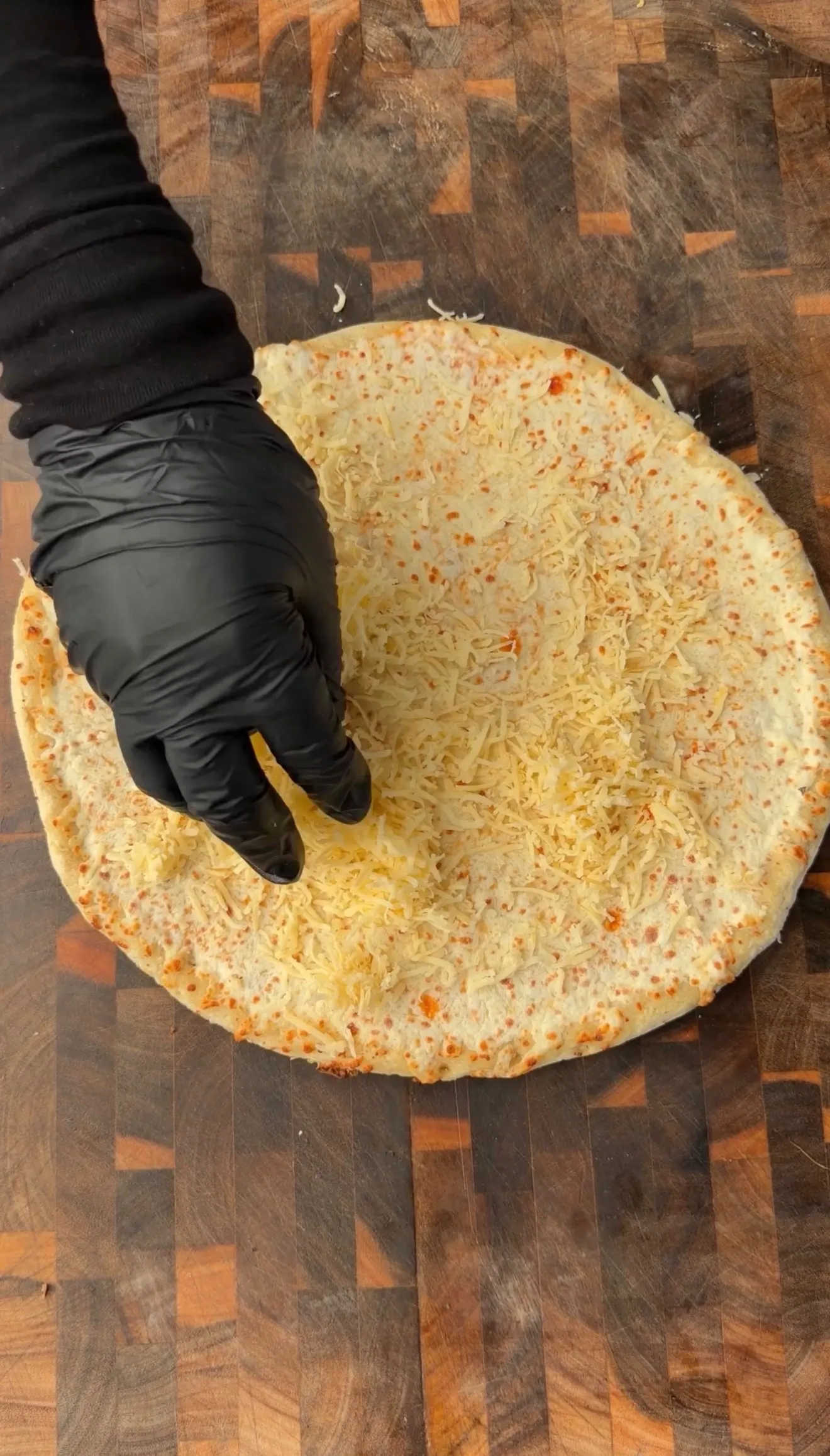 Hand in black glove preparing barbecue brisket pizza with melted cheese crust on wooden cutting board