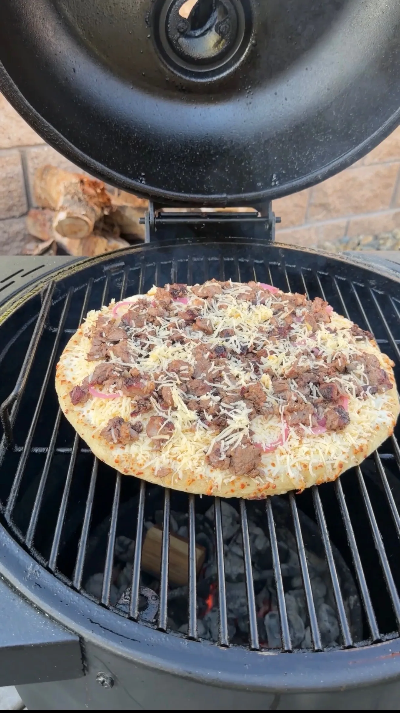 Barbecue brisket pizza with melted cheese cooking on a round charcoal grill grates