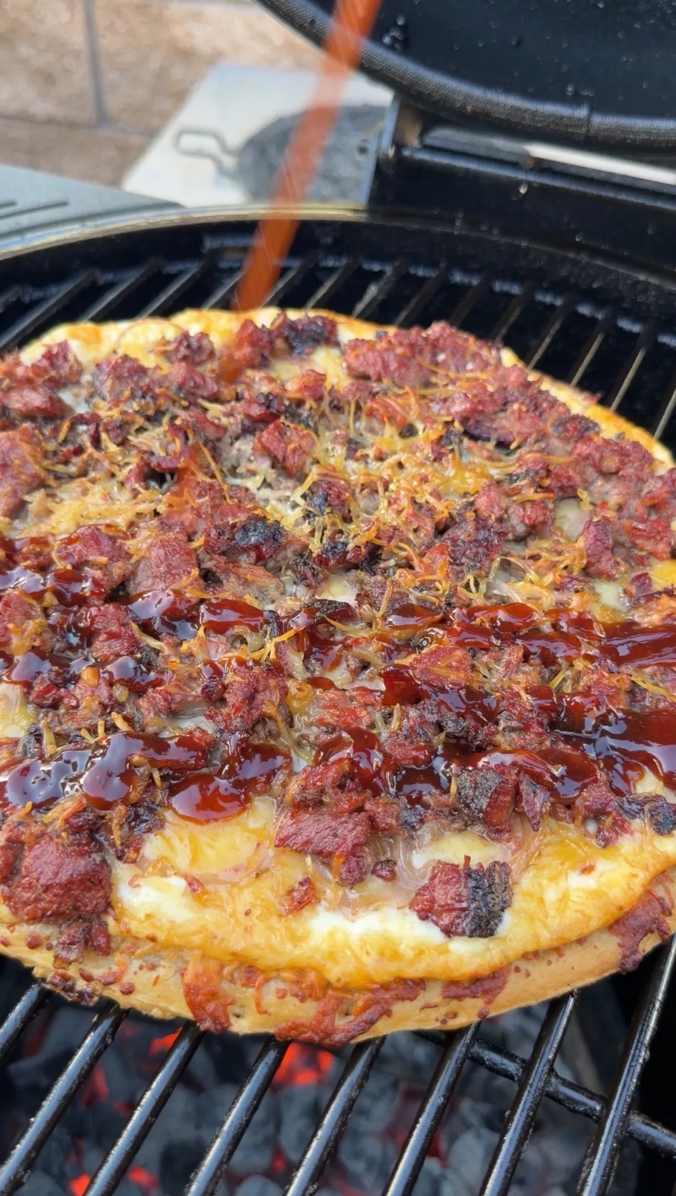 Barbecue brisket pizza with melted cheese and BBQ sauce cooking on outdoor grill grates