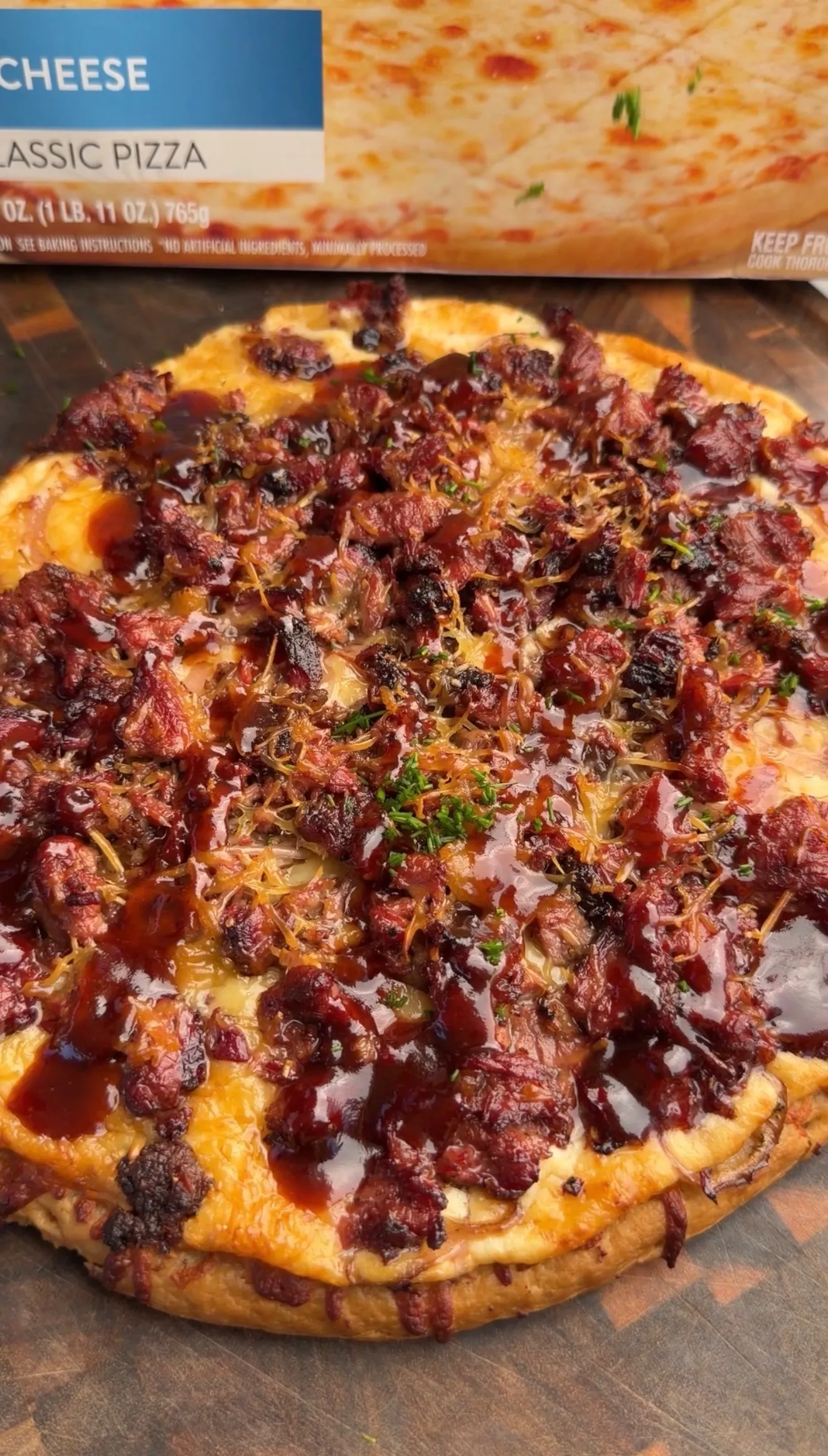Barbecue brisket pizza topped with crispy bacon, caramelized onions, and fresh herbs on wooden surface