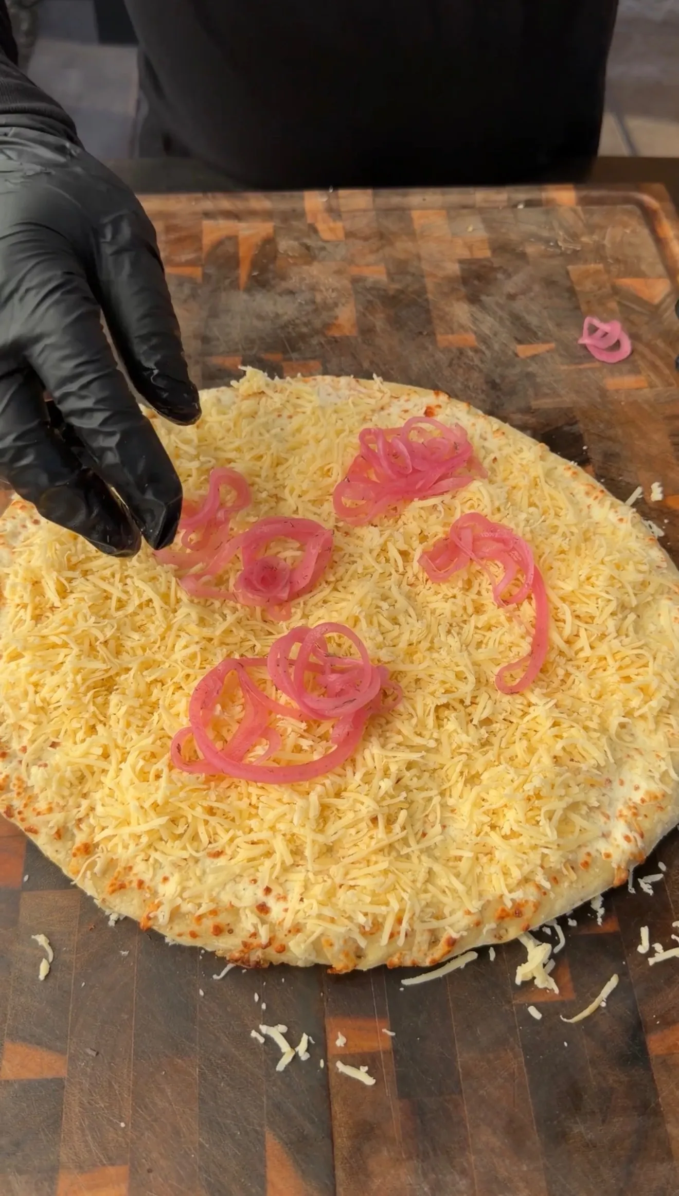 Barbecue brisket pizza topped with melted cheese and pickled red onions on wooden cutting board