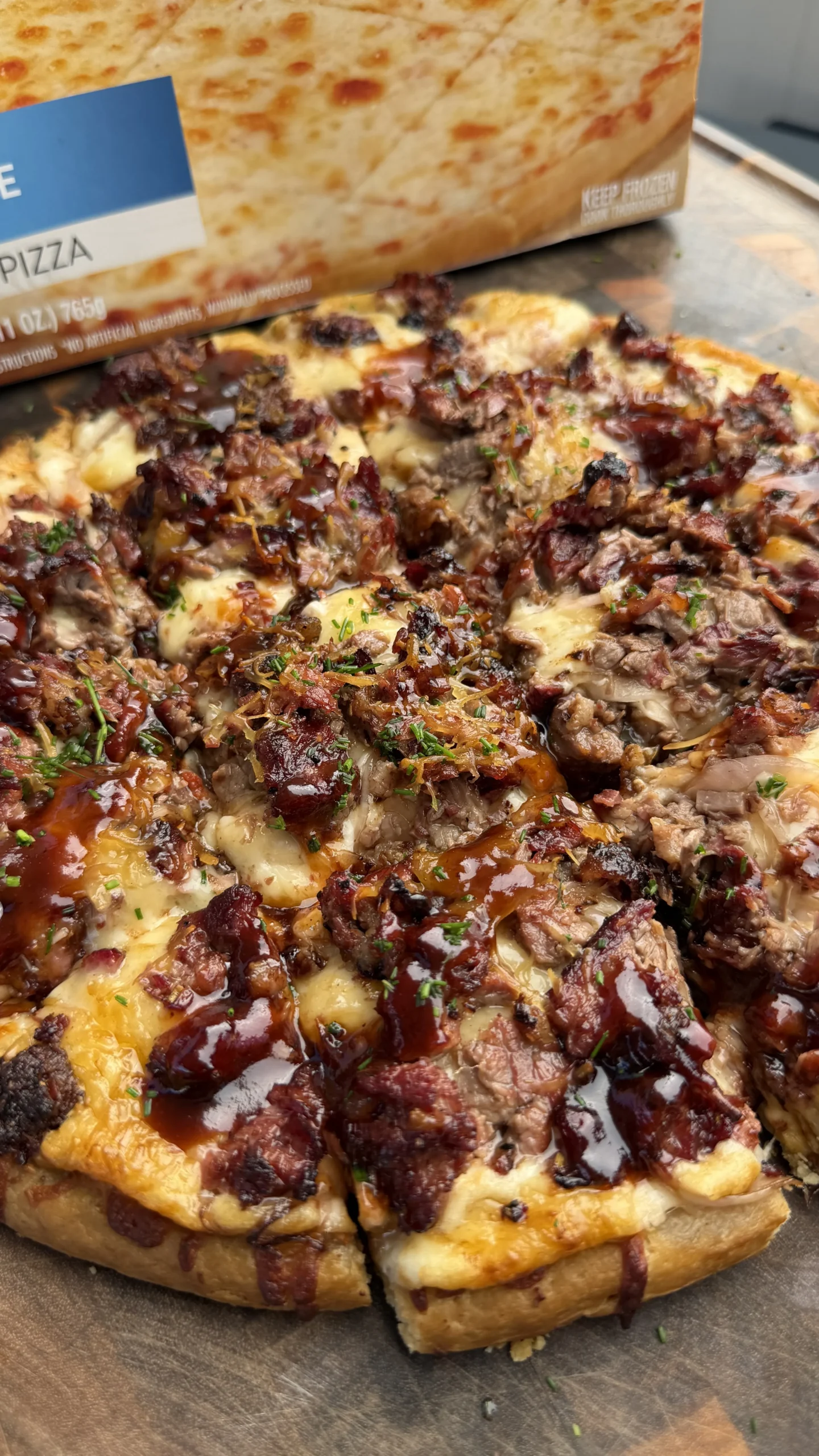 Sliced barbecue brisket pizza with melted cheese, caramelized onions, and herbs next to pizza box