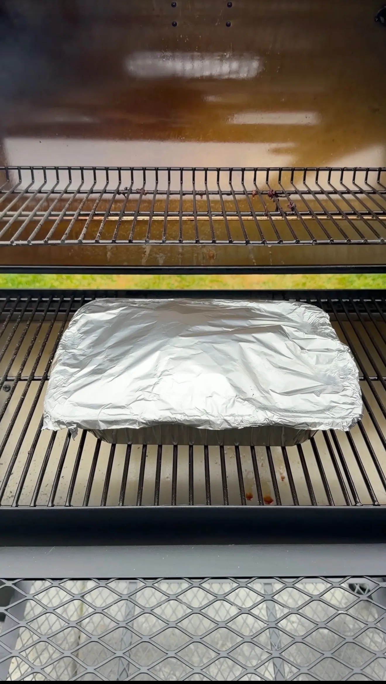 Hickory smoked beef plate ribs wrapped in aluminum foil resting on smoker grill grates