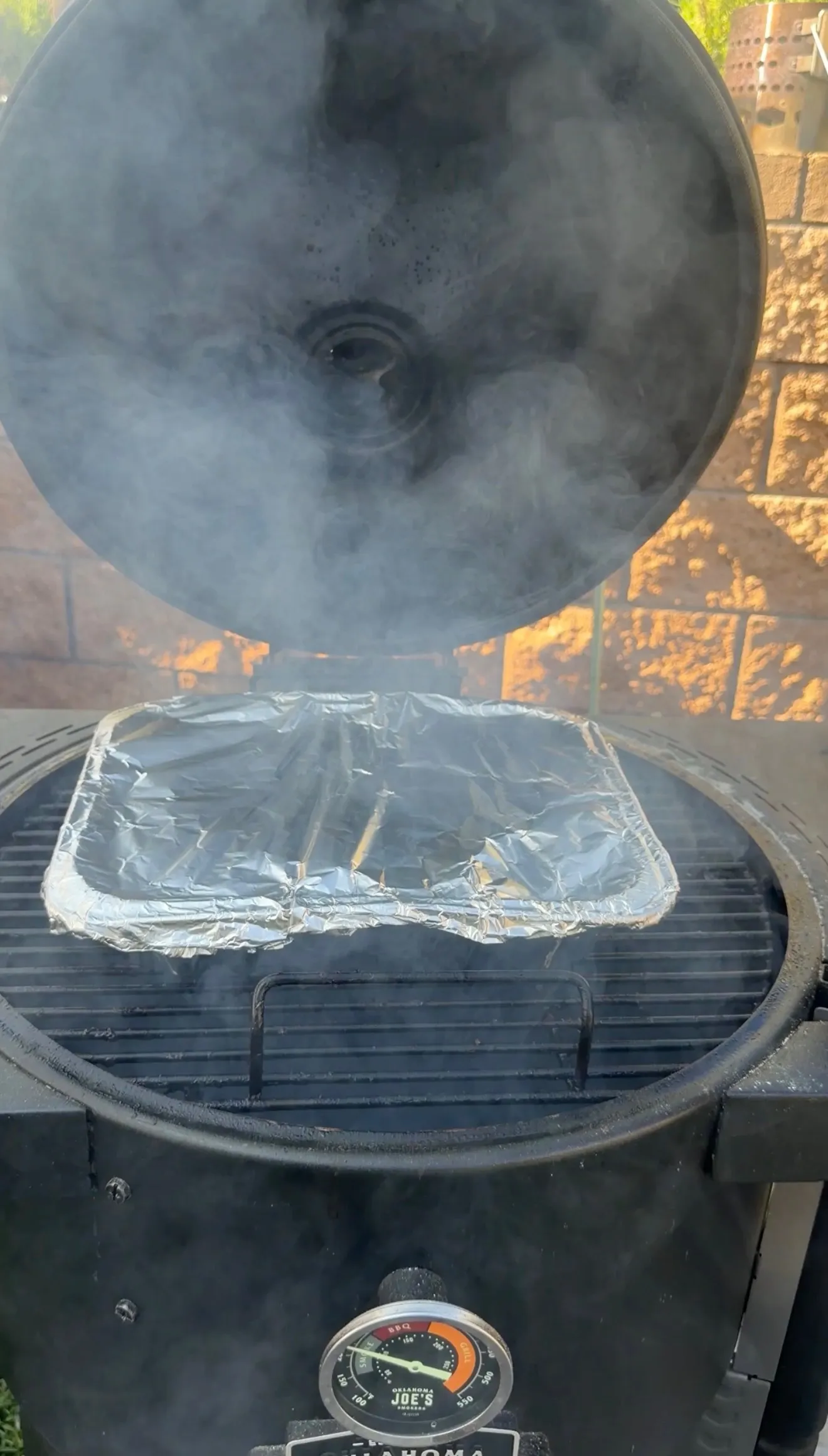 Beef ribs wrapped in foil smoking on a grill with temperature gauge, preparing molasses coffee burnt ends