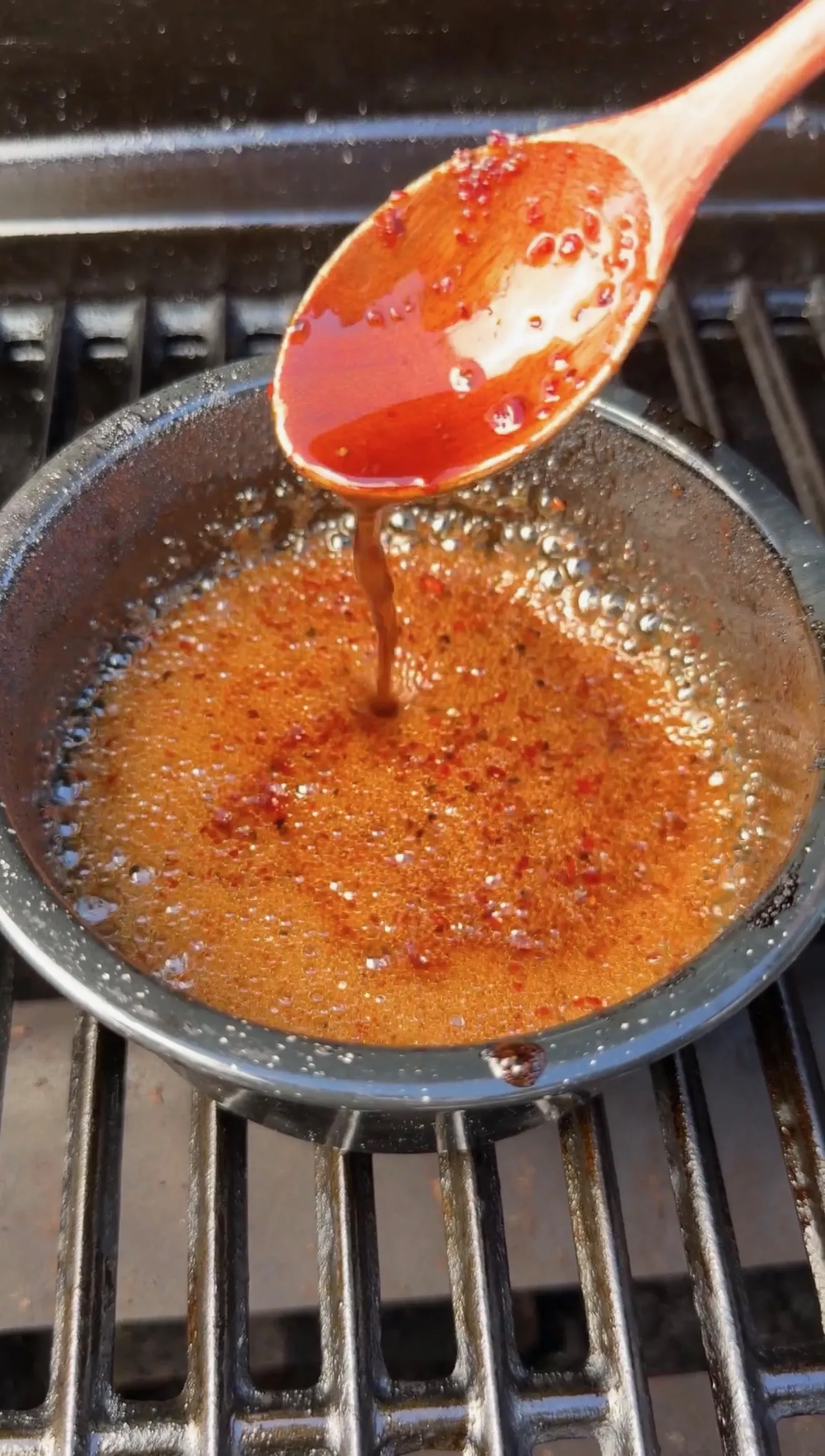 Bubbling bourbon glaze being stirred with wooden spoon in pan on grill grates