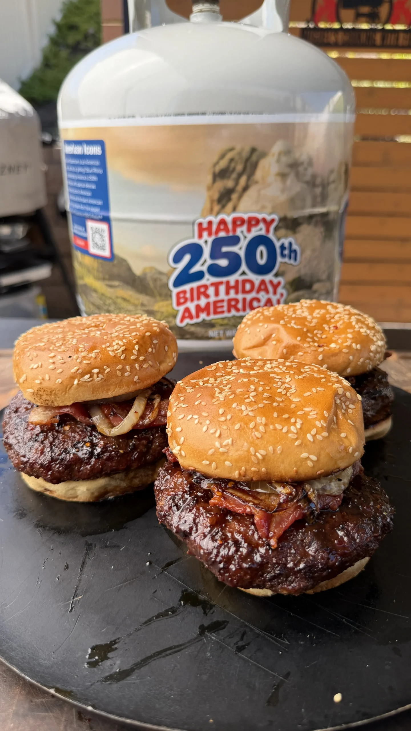 Three bourbon glazed bison burgers with caramelized onions on sesame seed buns, grilled on cast iron griddle