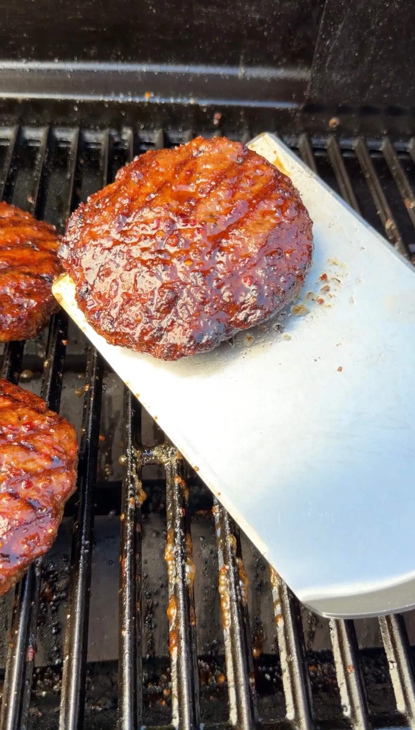 Bourbon glazed bison burger patties with caramelized glaze cooking on barbecue grill grates with spatula