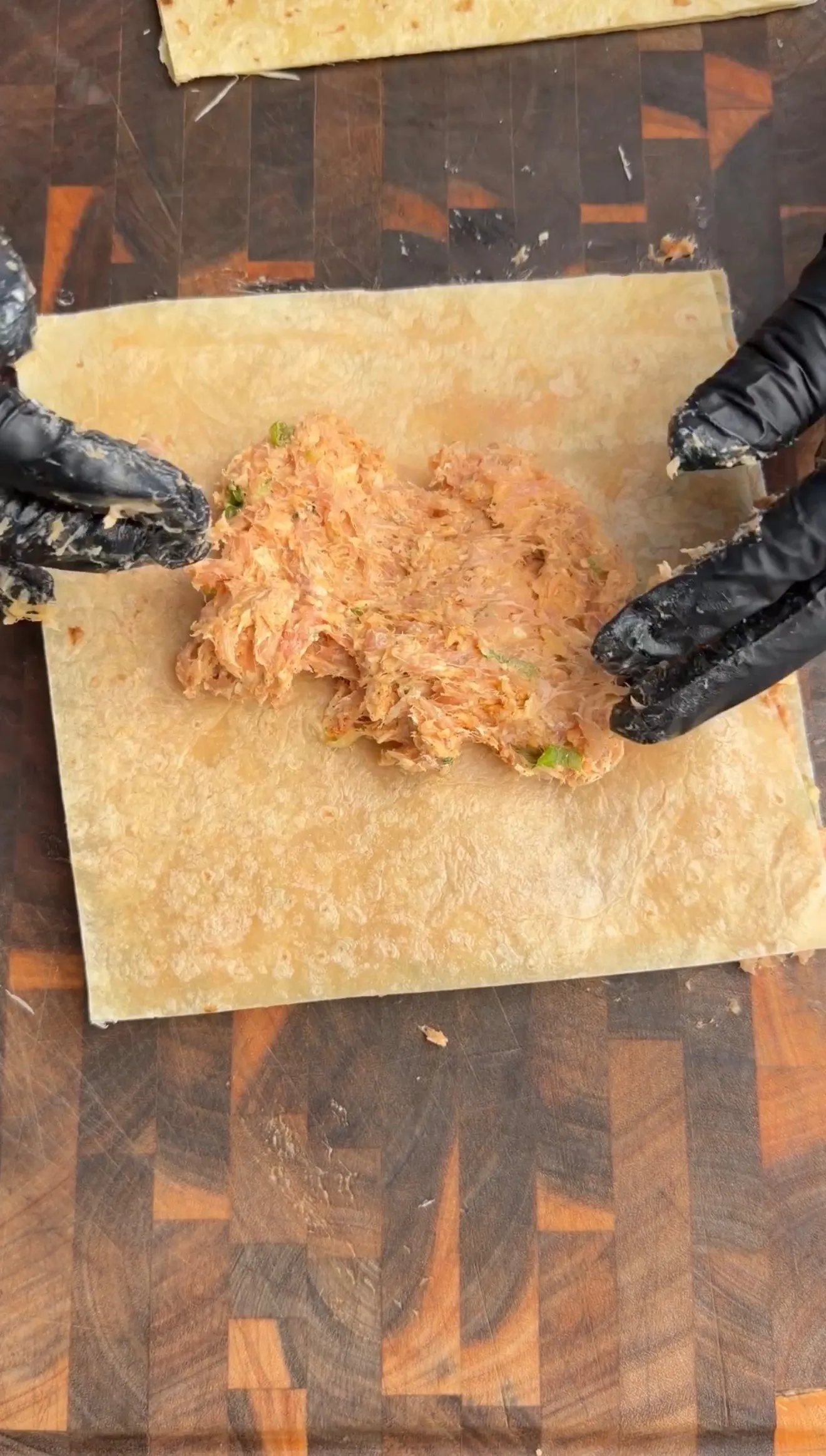 Shredded buffalo chicken mixture with herbs spread on flour tortilla for kebab preparation