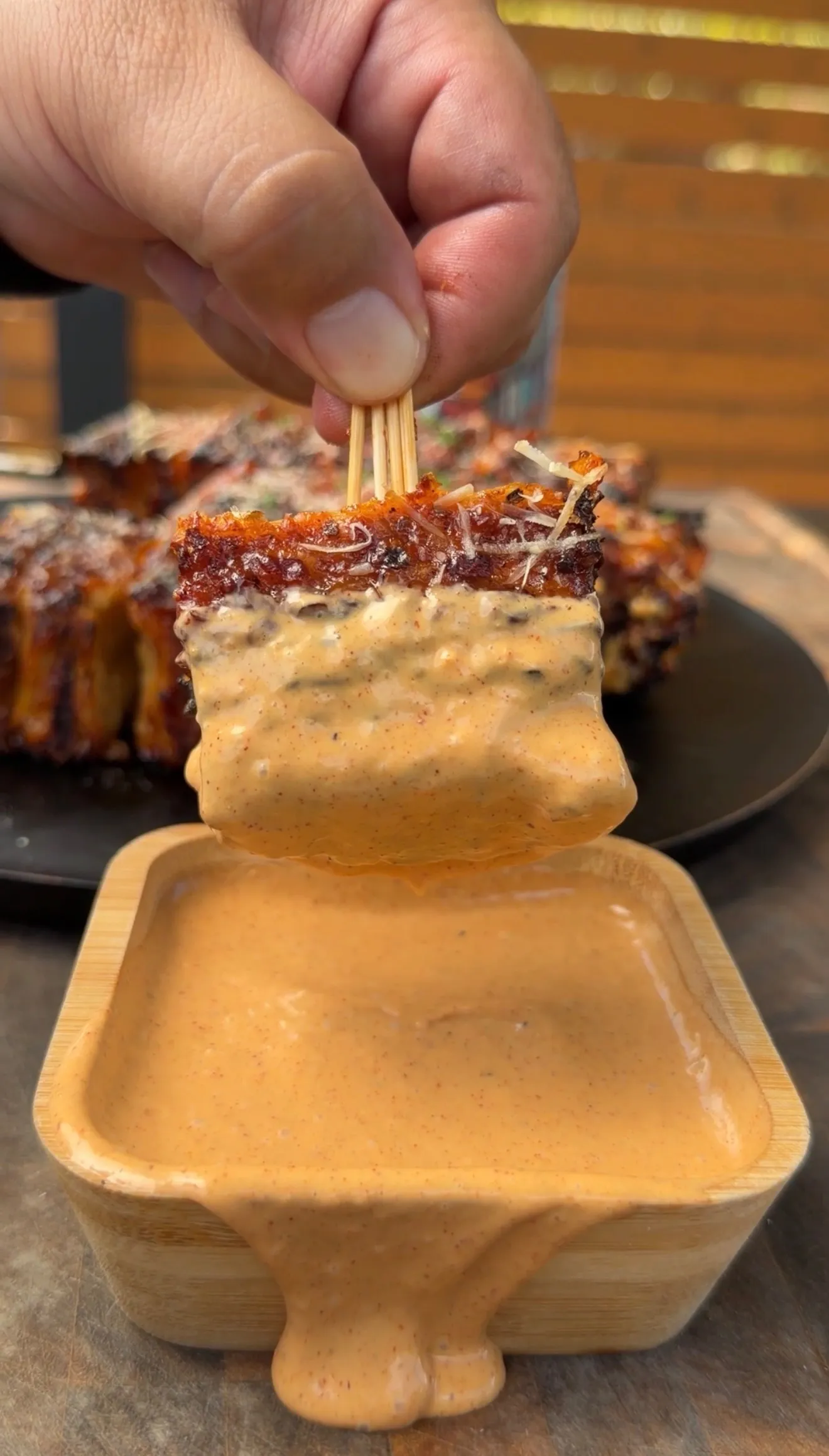 Buffalo chicken tortilla kebab being dipped into creamy sauce in wooden bowl with more kebabs on plate