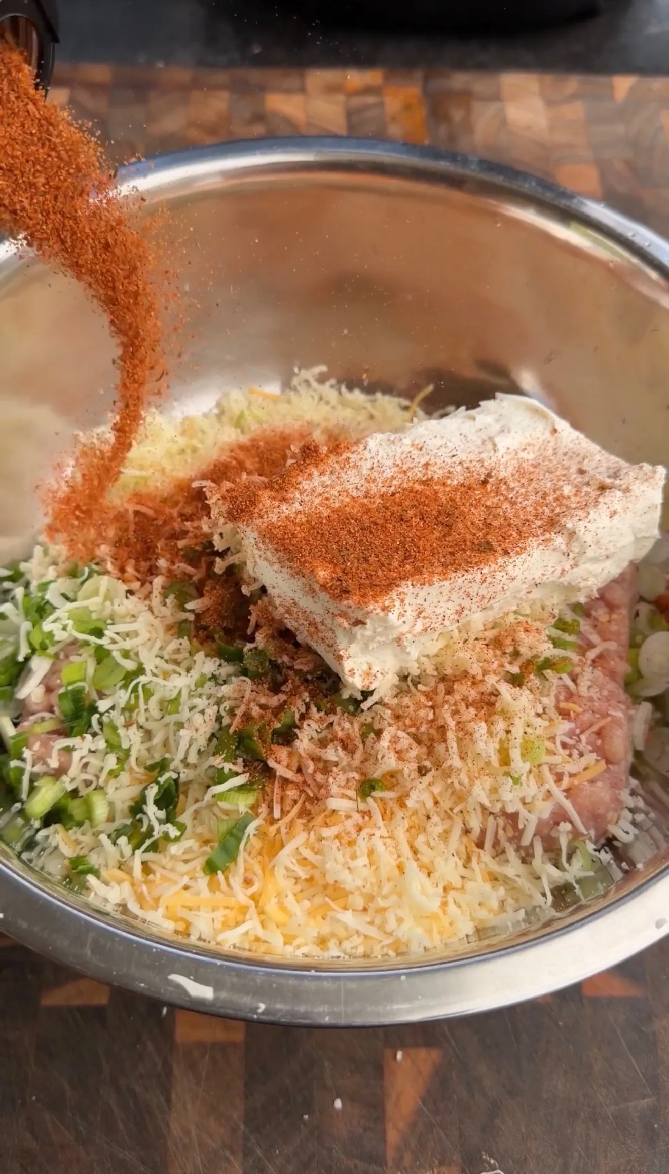 Buffalo chicken mixture in metal bowl with paprika spice being sprinkled on top during recipe preparation