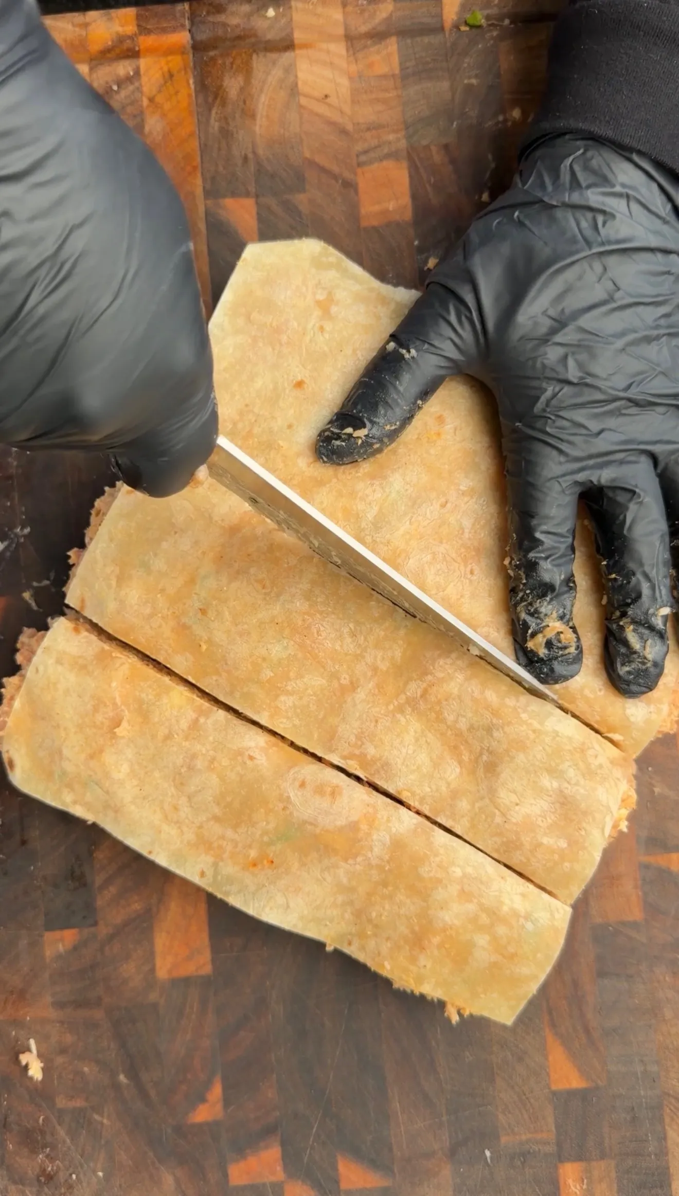 Hands in black gloves slicing buffalo chicken tortilla kebabs on a wooden cutting board with knife