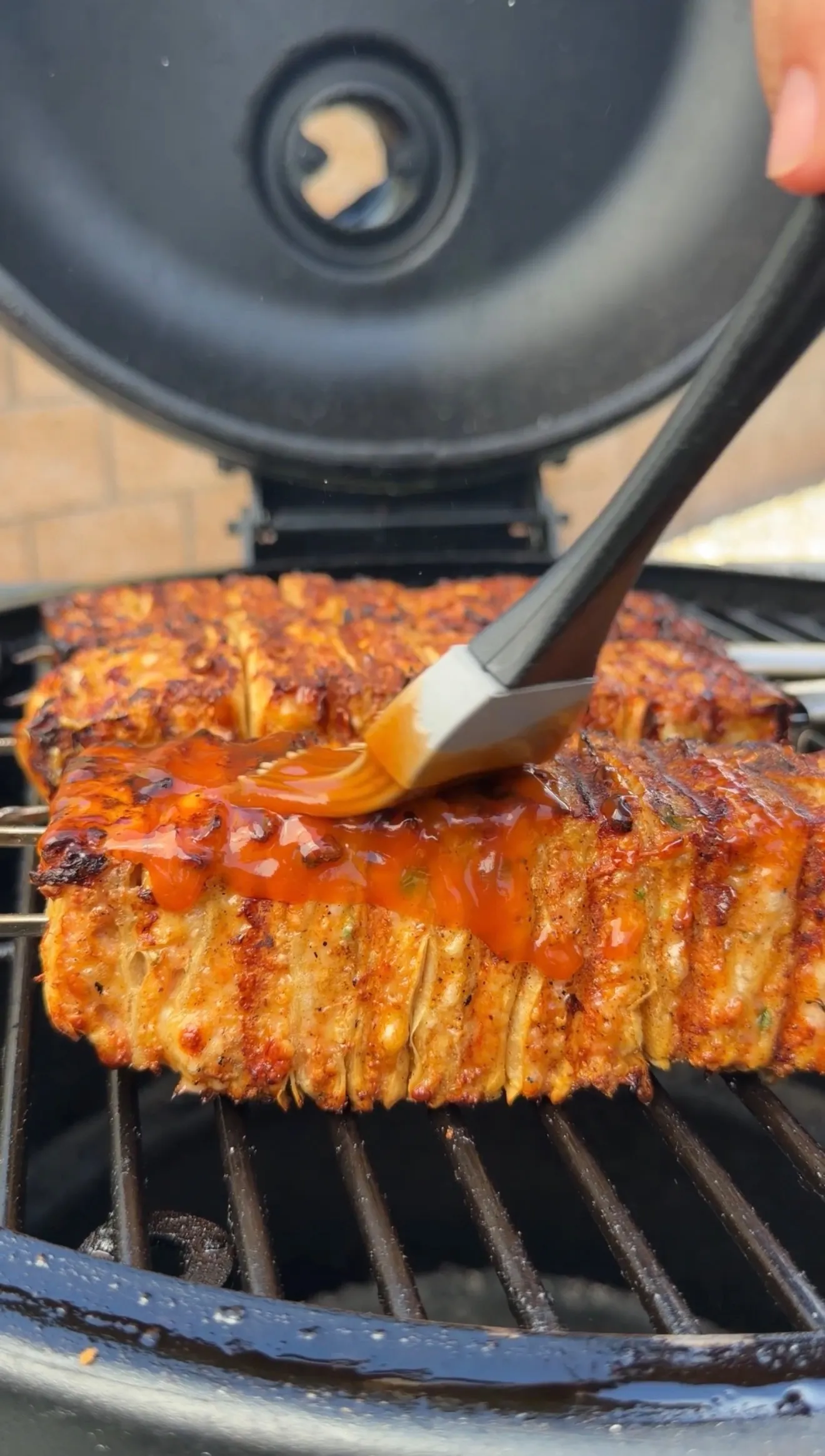 Buffalo chicken tortilla kebabs being brushed with orange buffalo sauce while grilling on outdoor barbecue grates