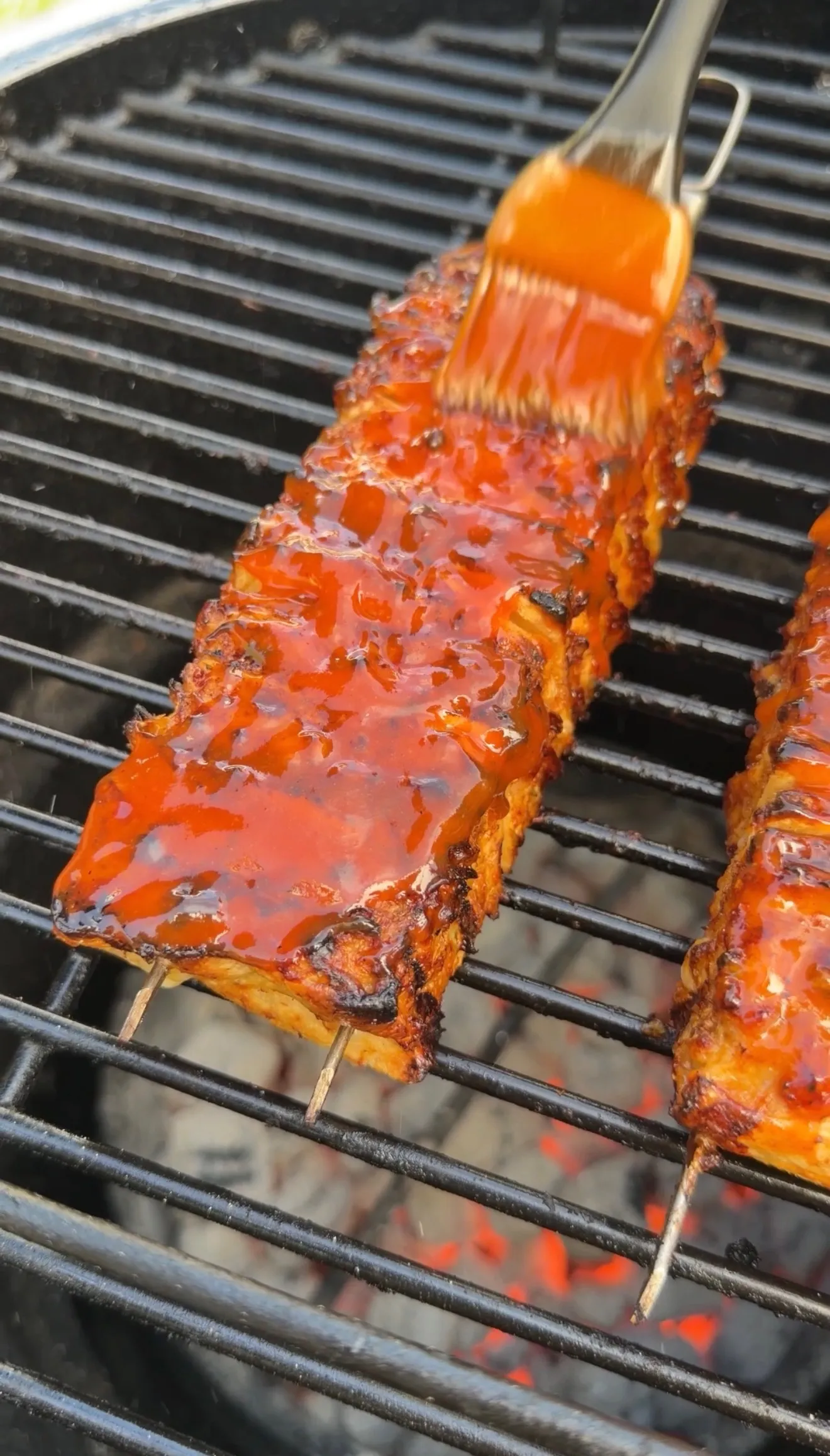 Buffalo chicken tortilla kebabs on grill grates being basted with orange buffalo sauce using a brush