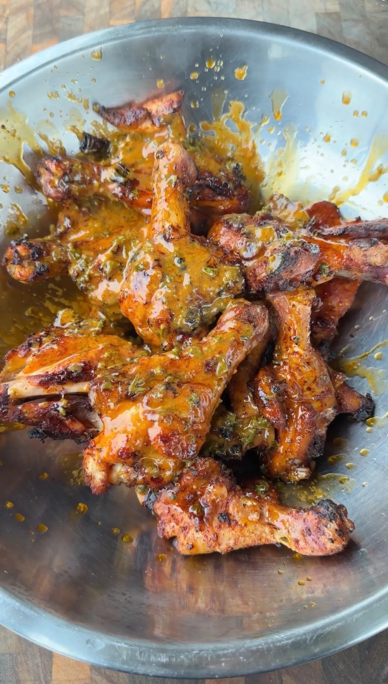 Grilled chicken drumsticks tossed in butter chili lime sauce in a stainless steel mixing bowl