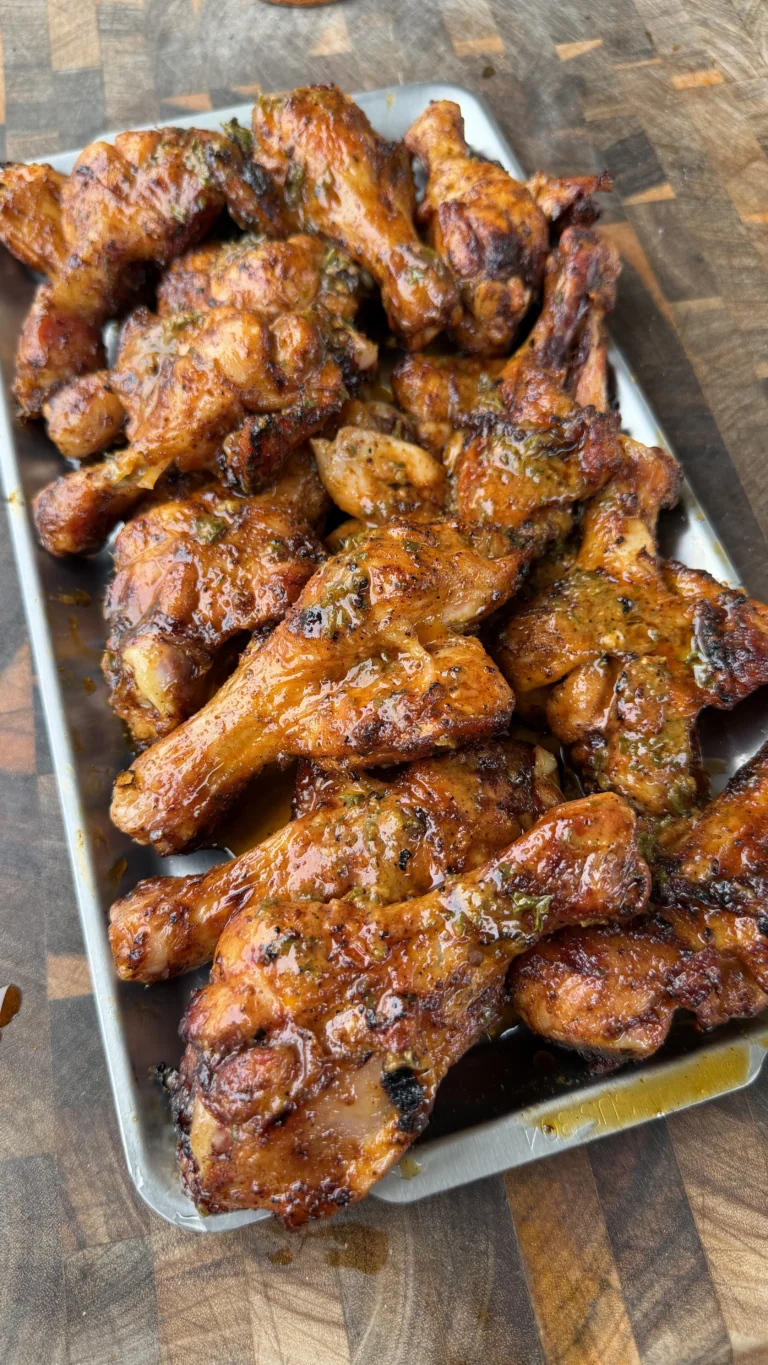 Glazed butter chili lime grilled chicken drumsticks piled on a metal tray on a wooden cutting board